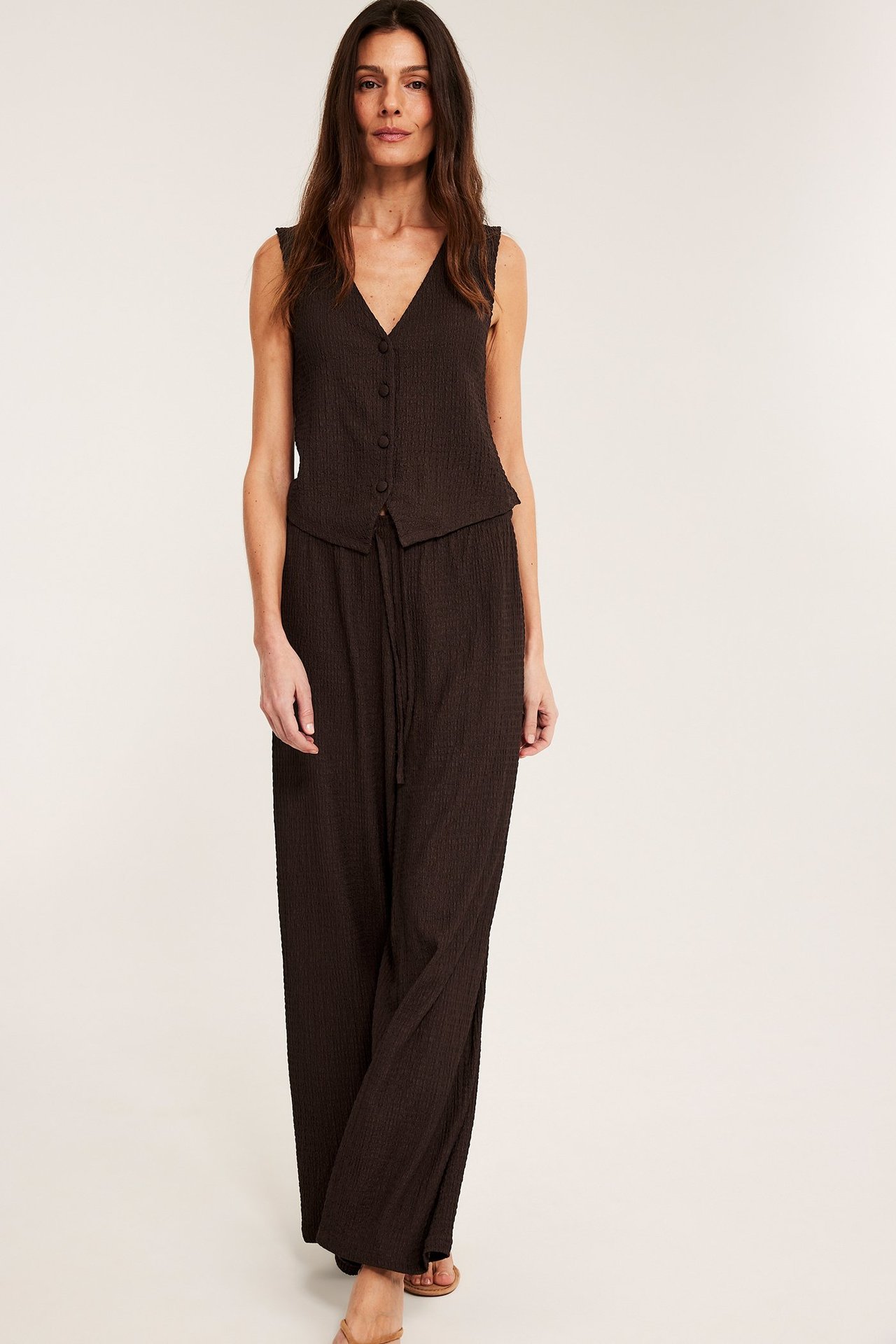 Framifrån, kvinna i mörkbruna pull-on byxor med dragsko och matchande väst i strukturerad jersey.