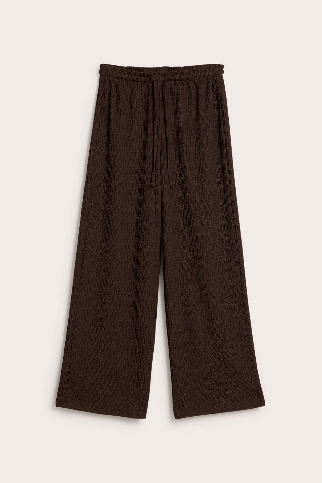 Edestä tummanruskeat leveälahkeiset housut, joissa kiristysnyöri ja joustinneuleinen struktuuri.