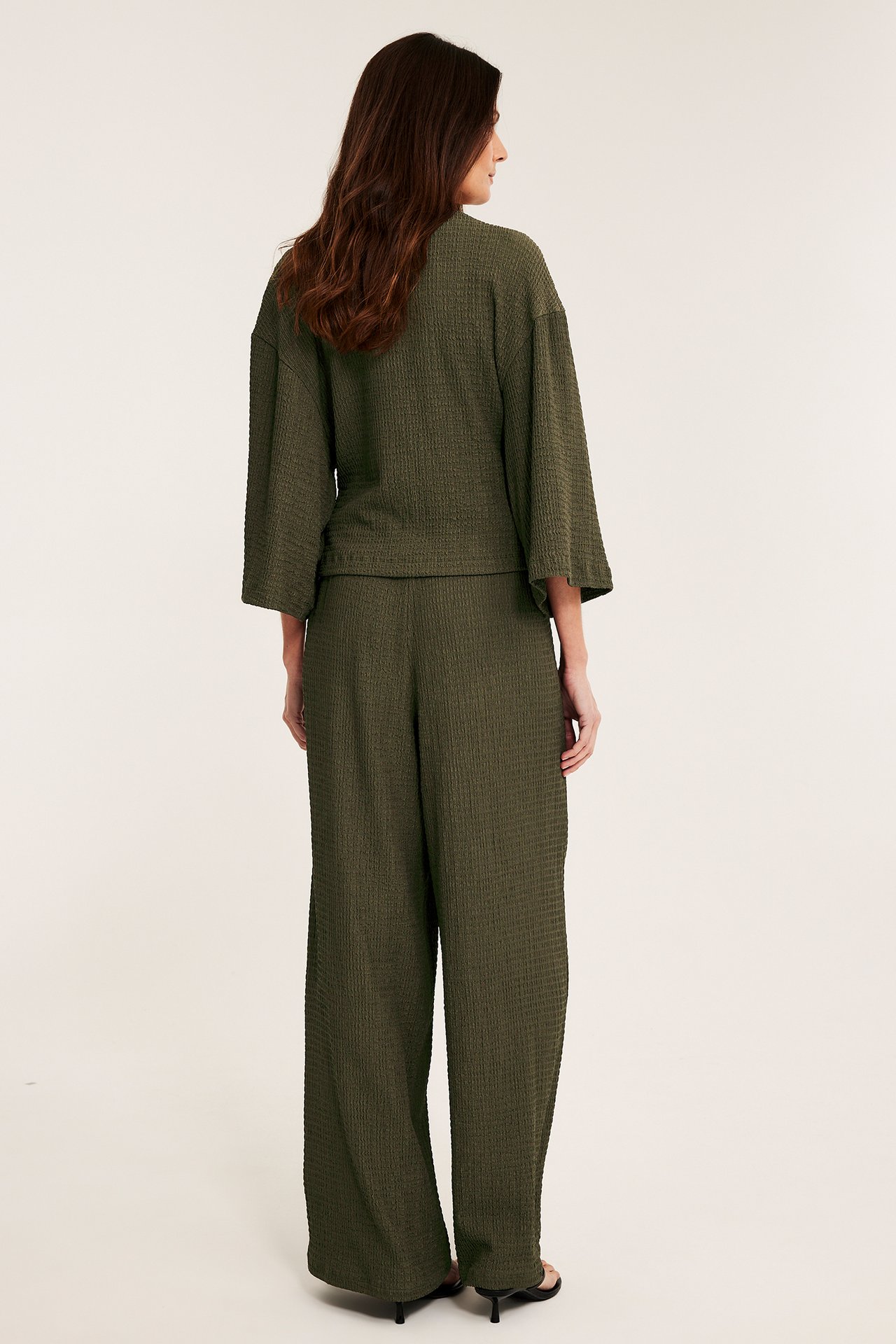 Naisen selkäpuoli: vihreät leveälahkeiset vetohousut ja yhteensopiva strukturoitu trikoo-kietaisutoppi.