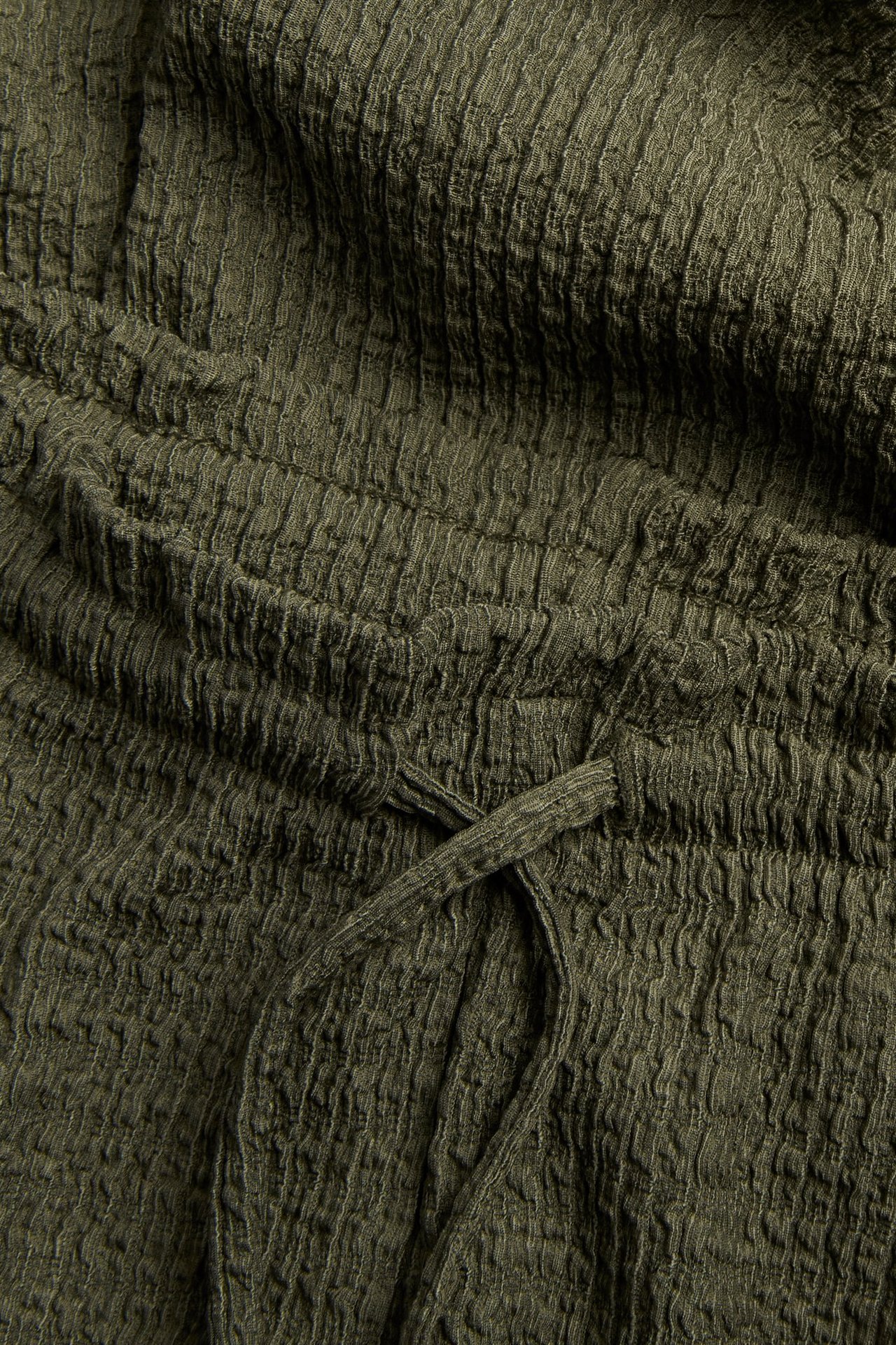 Lähikuva vihreistä housuista, joissa on teksturoitu jersey-laatu ja nyöritys vyötäröllä.