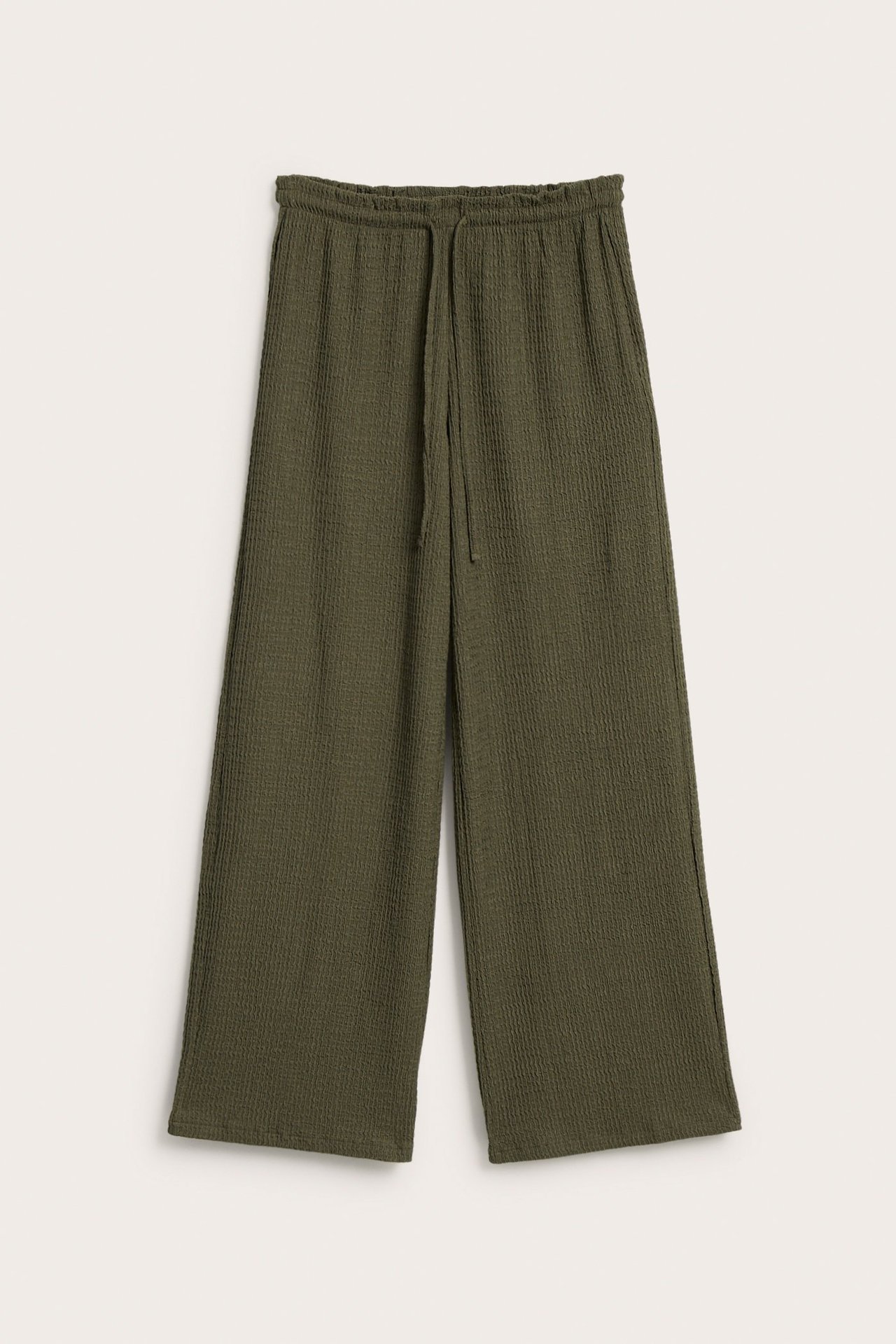 Frontvy av gröna vida byxor i strukturerad jersey med dragsko och volangkant i midjan.