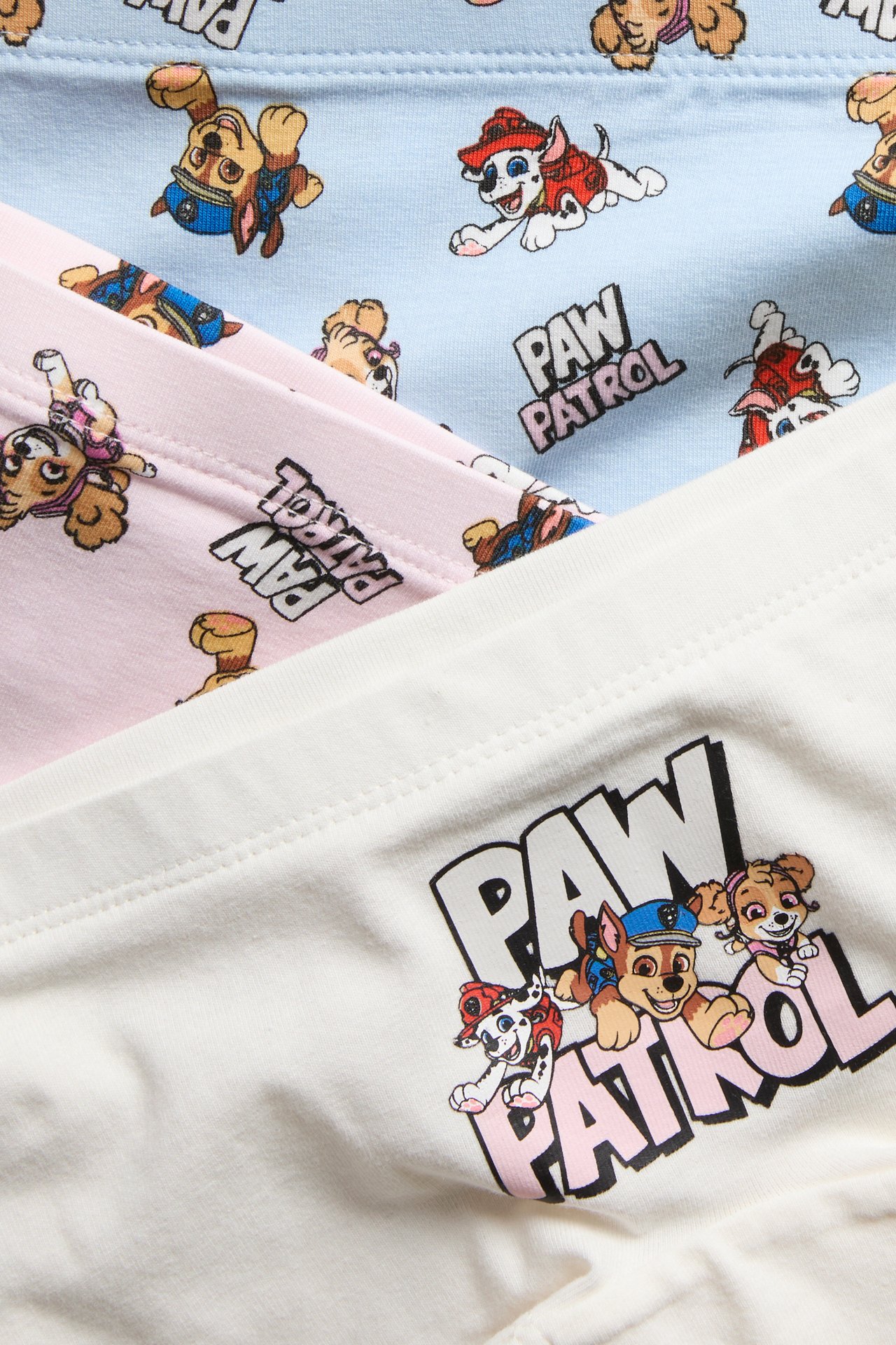 Nærbilde av hvite barnebokser med Paw Patrol-logo, stablet med rosa og blå mønstrede bokser.