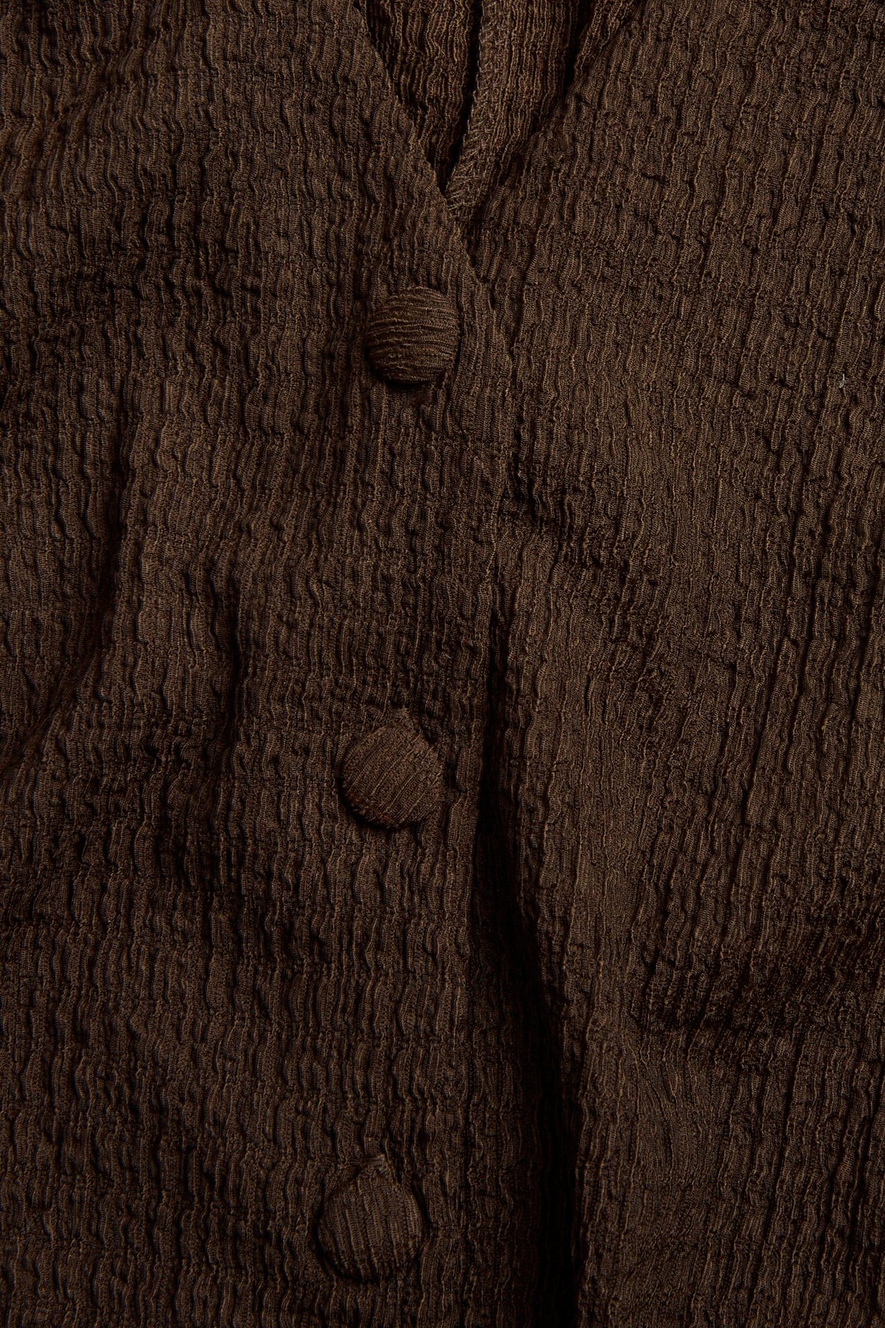 Zbliżenie ciemnobrązowej strukturalnej kamizelki z dżerseju z materiałowymi guzikami.