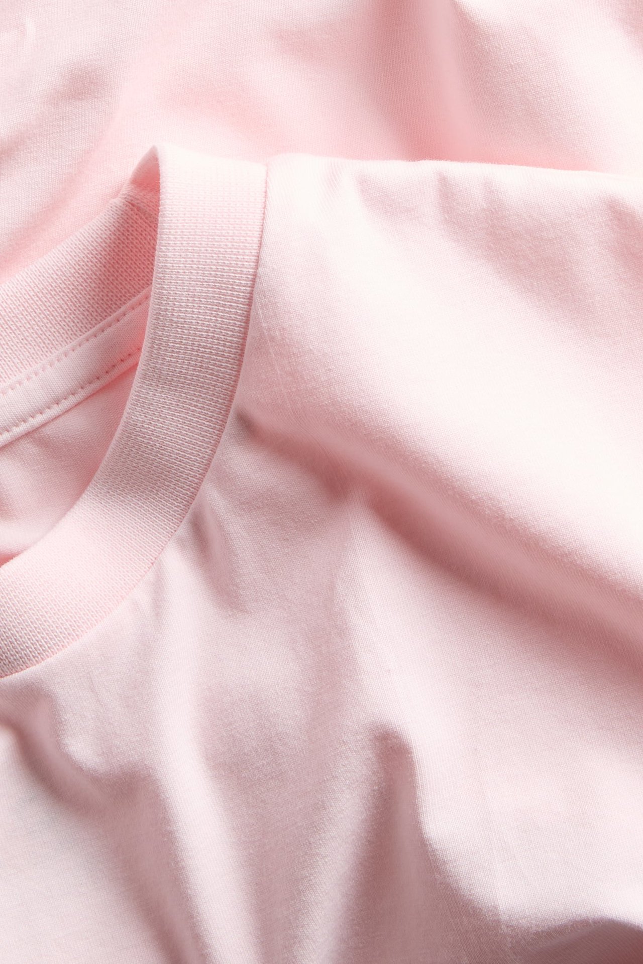 Zbliżenie jasnoróżowej, gładkiej koszulki z mieszanki bawełny z prążkowanym okrągłym dekoltem.