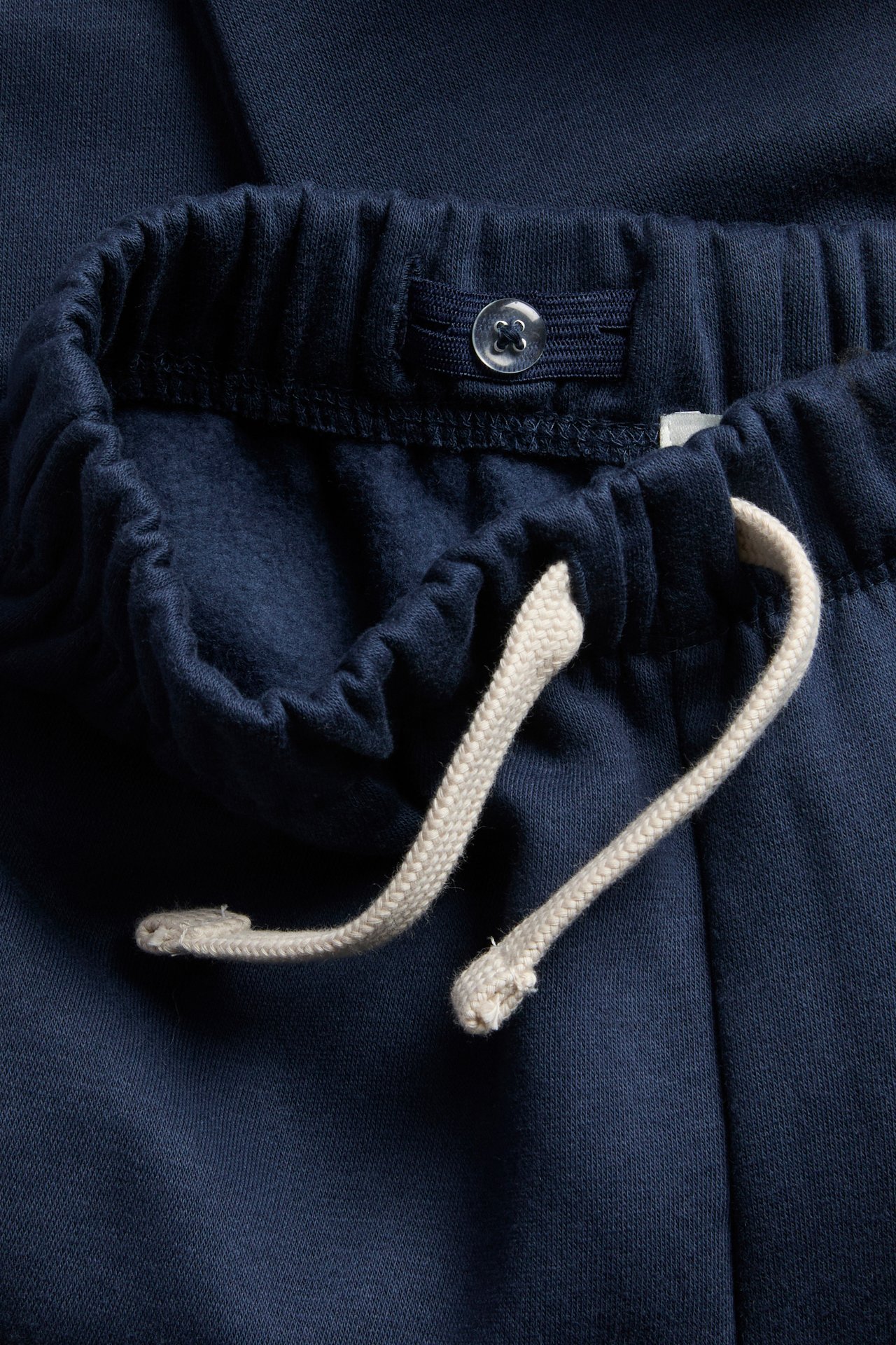 Nærbilde av mørkeblå joggebukse med elastisk midje, justerbar snøring og innerknapp.