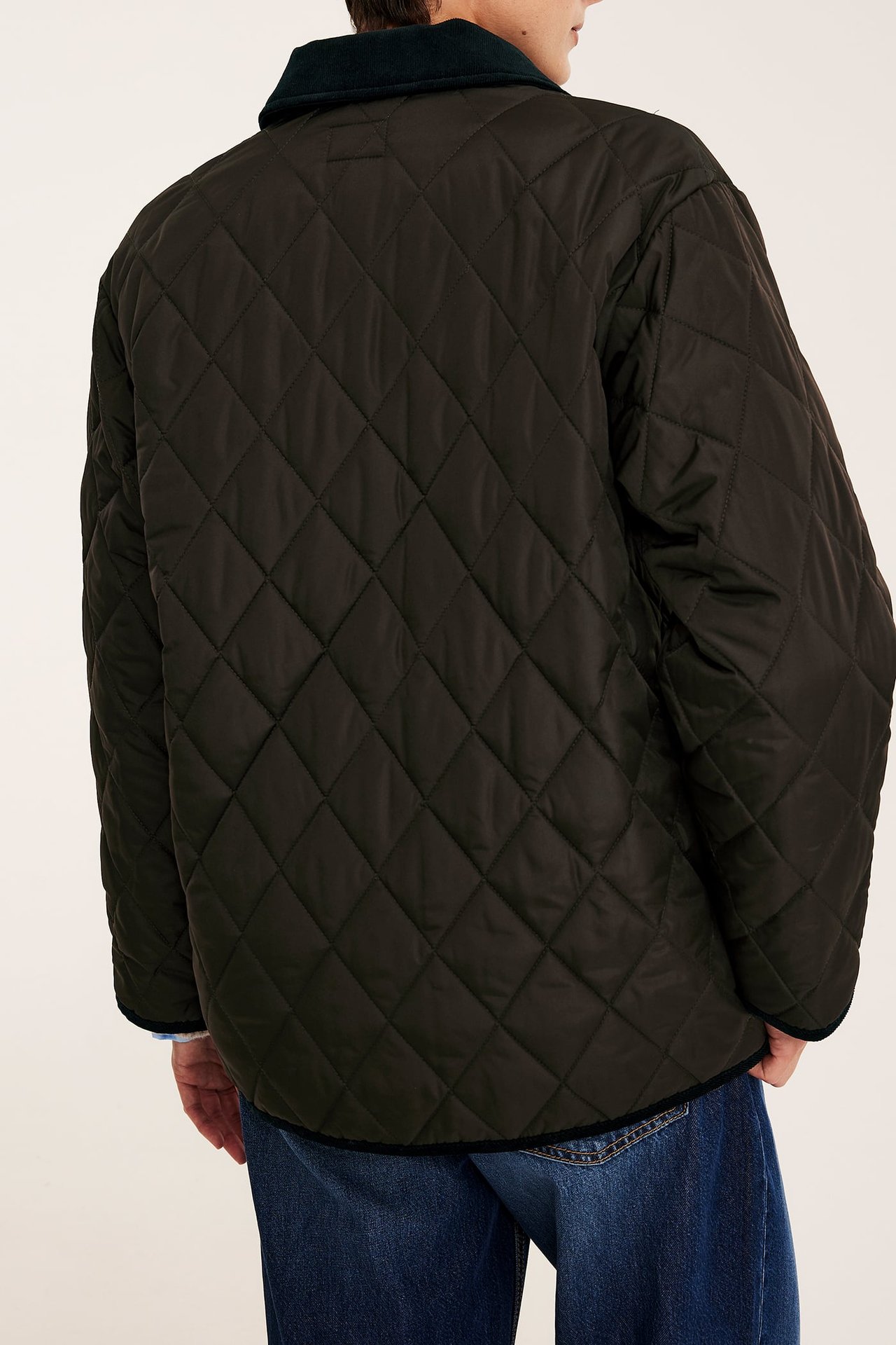 Bakfra av mann i mørkegrønn vattert jakke med kordfløyelkrage, stylet med jeans.