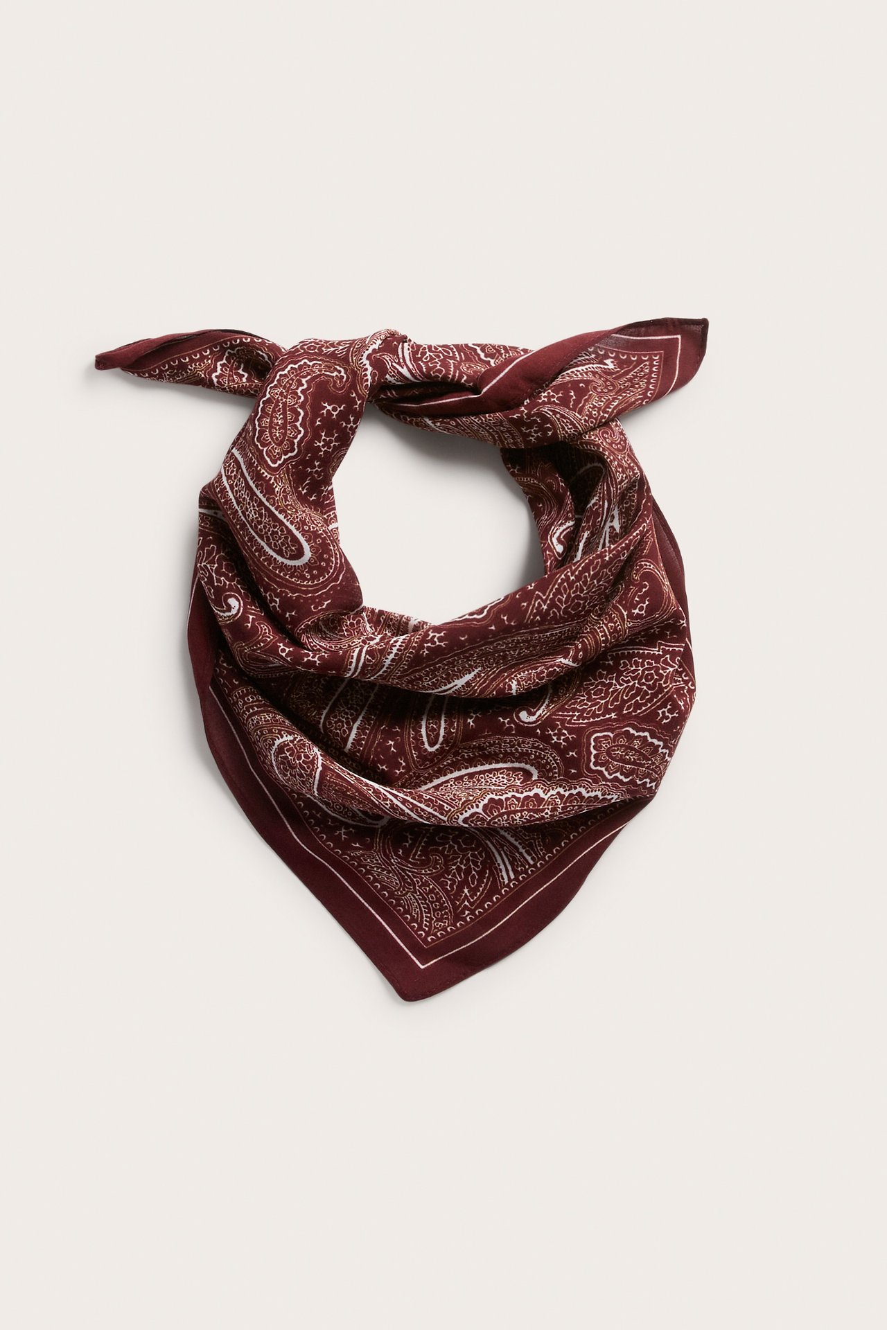 Ovanifrån vy av en vinröd bandana med vitt paisleymönster, vikt till en triangel.