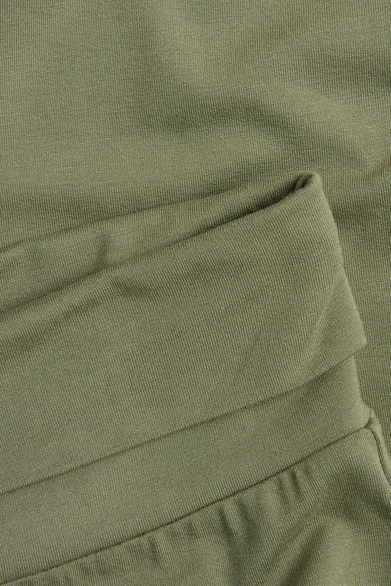 Zbliżenie na ciemnozielone, jednolite legginsy flare z prążkowanym, wywijanym pasem.