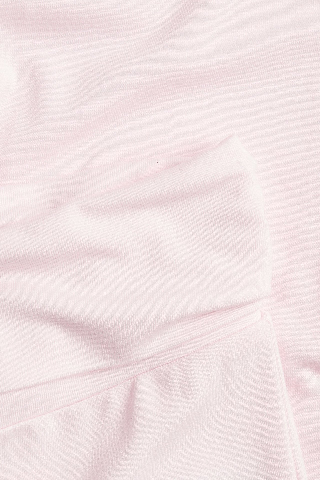 Lähikuva vaaleanpunaisista levenevistä leggingseistä, joissa alas käännettävä vyötärö, esitellen pehmeää ribbineulosta.