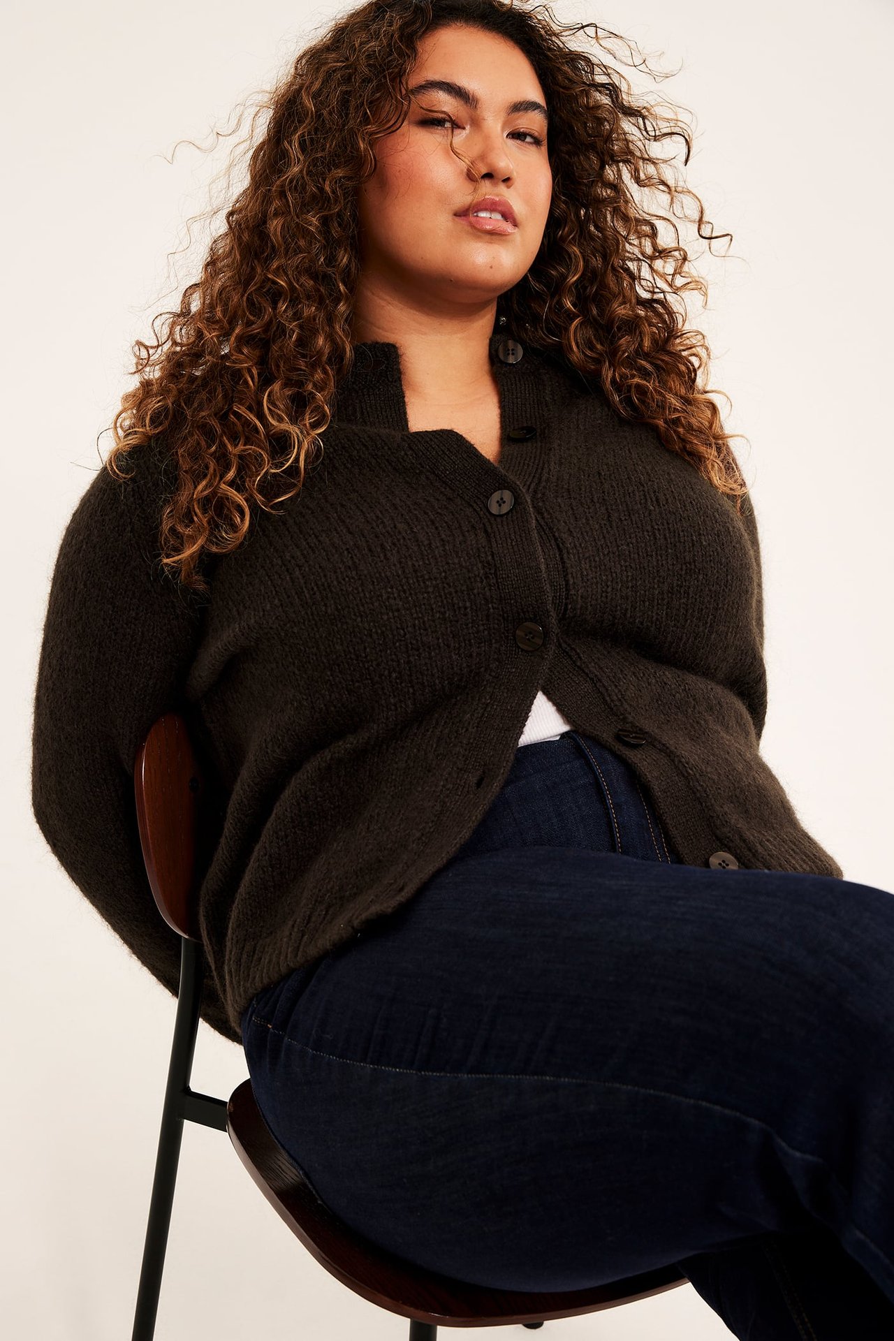 Front: Kvinne i mørk brun ribbet V-hals knappet cardigan og mørk blå jeans.