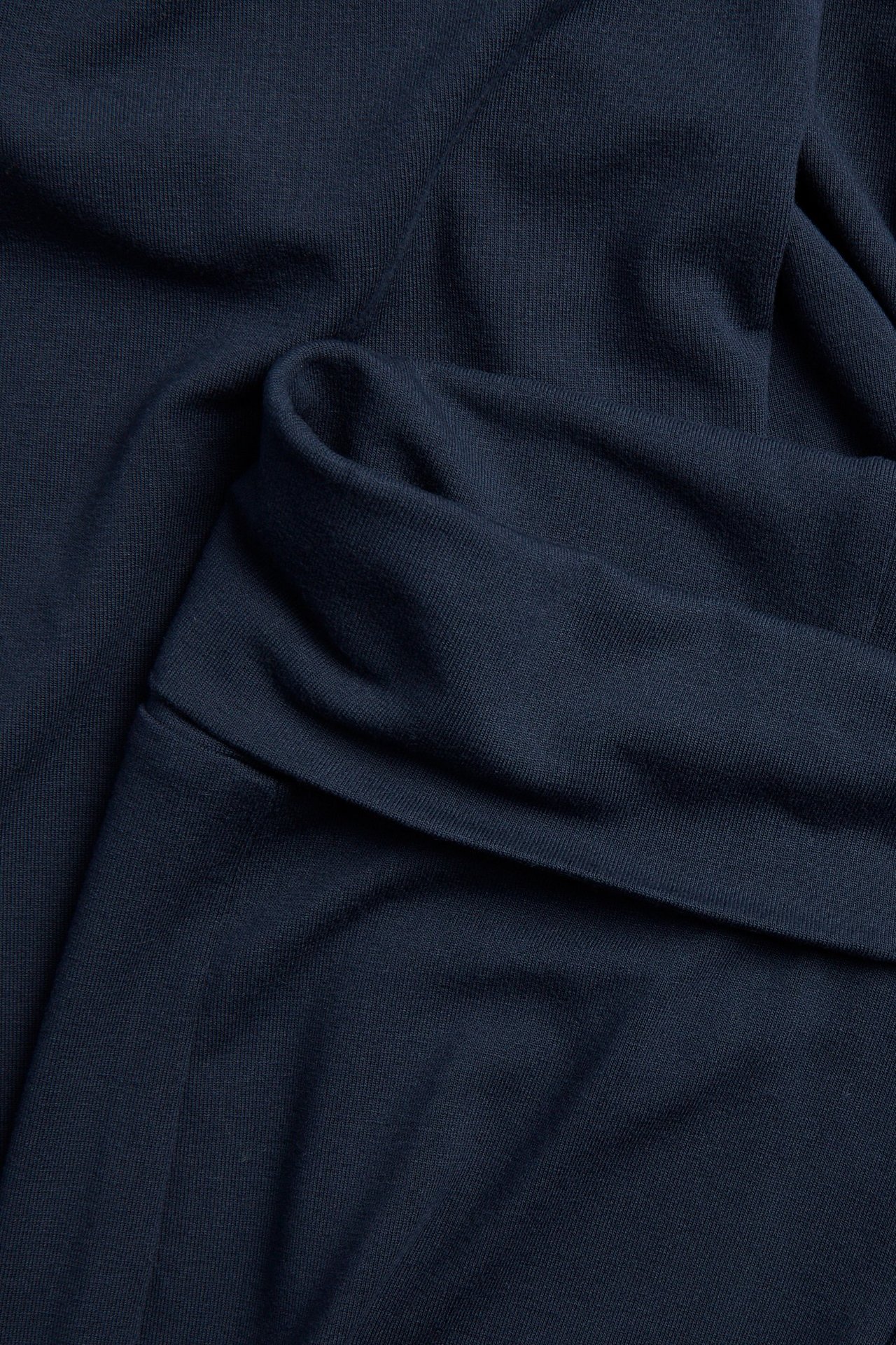 Zbliżenie ciemnoniebieskich legginsów z rozszerzanymi nogawkami i składanym pasem, z miękkiego dżerseju.