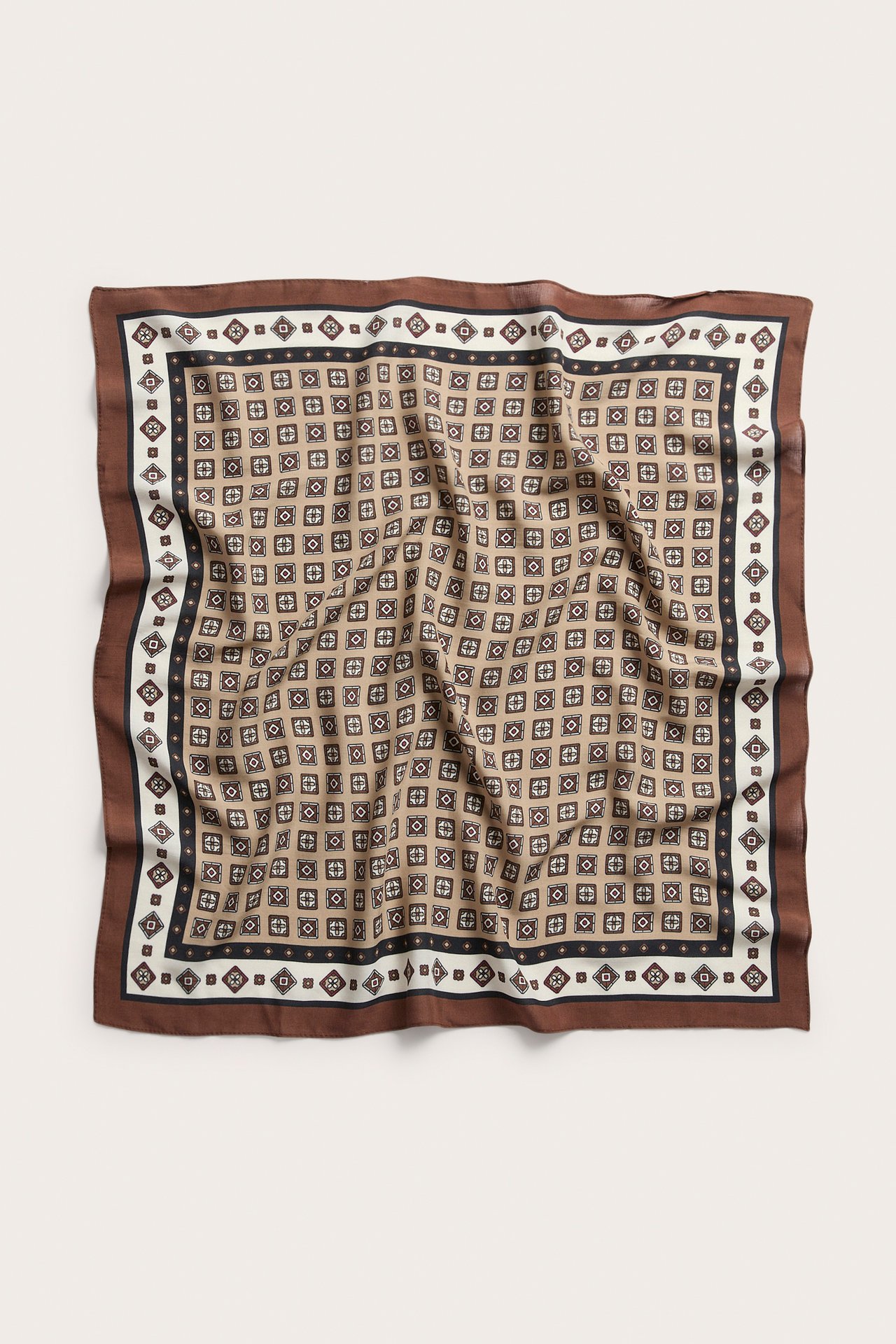 Ovanifrån vy av en vikt brun, beige, svart och vit mönstrad sidenscarf.