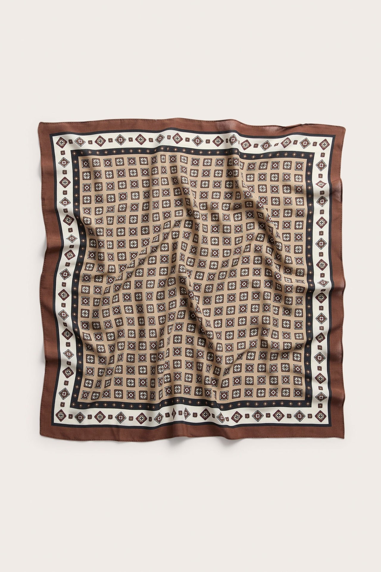 Toppvisning av et foldet brunt, beige, svart og hvitt mønstret silkeskjerf.
