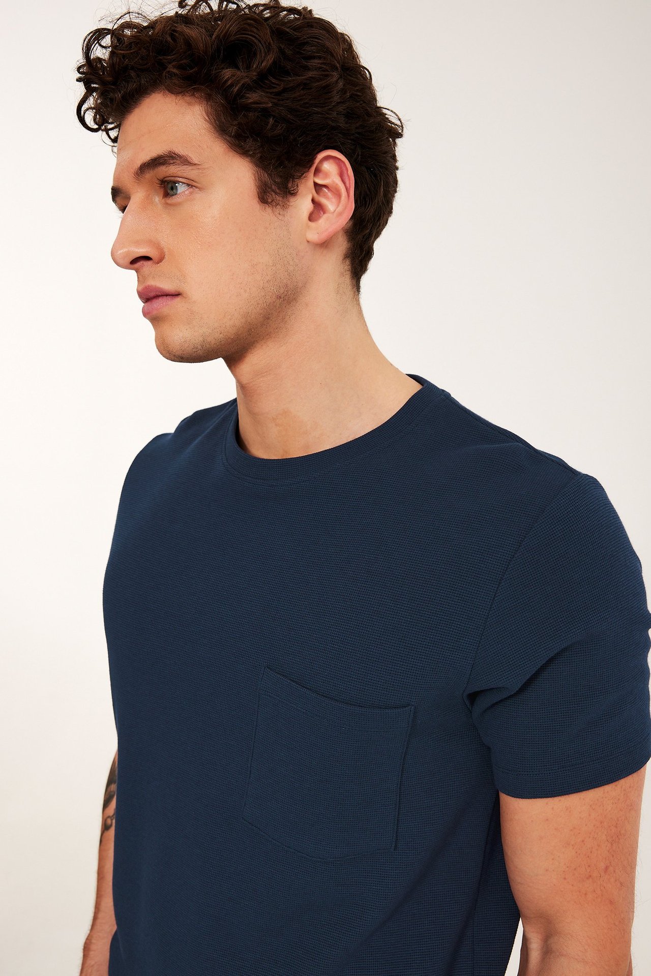 Widok z boku mężczyzny w granatowym teksturowanym t-shircie z okrągłym dekoltem i kieszenią.