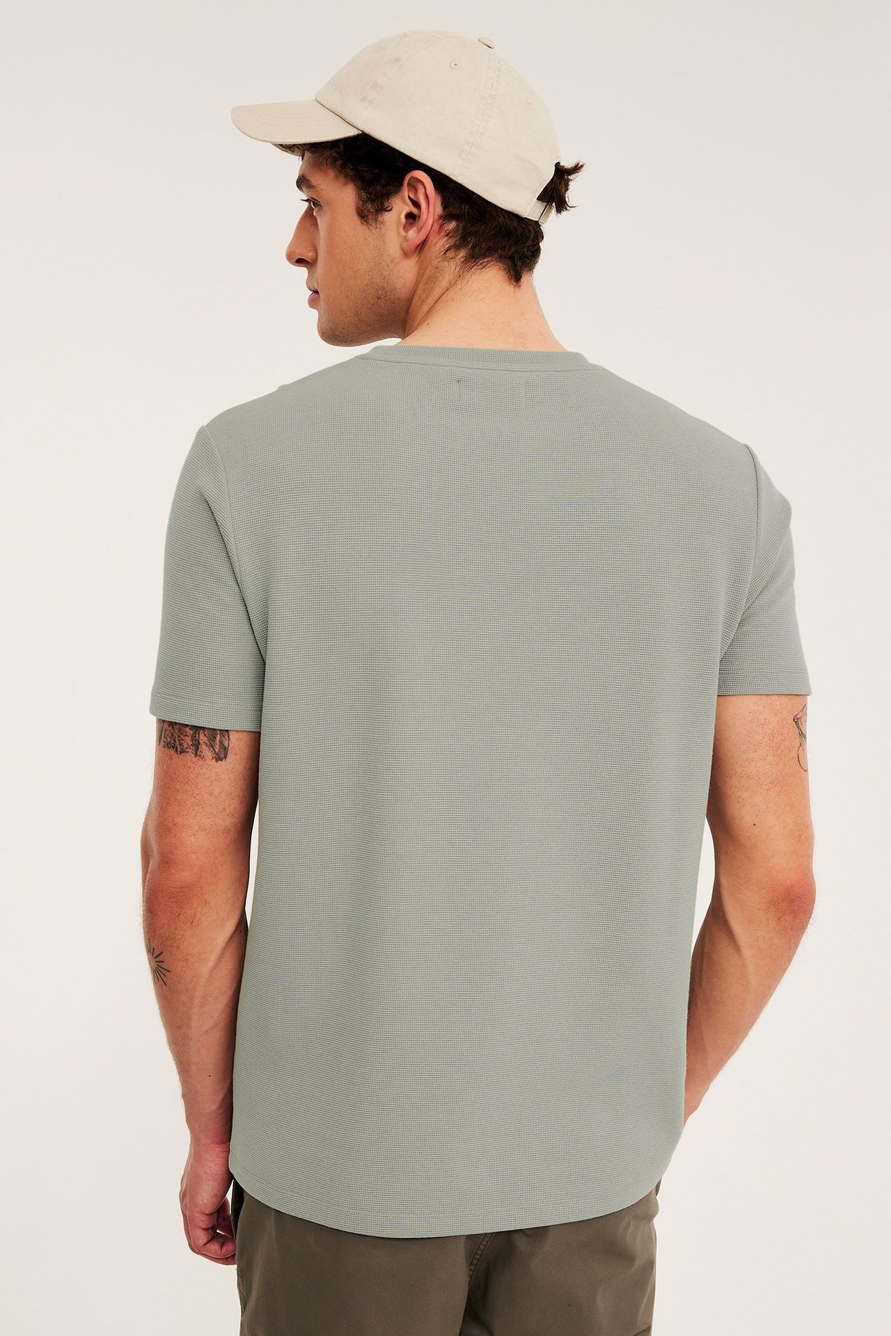 Mies takaa, yllään vaaleanvihreä strukturoitu regular fit T-paita ja beige baseballlippis.