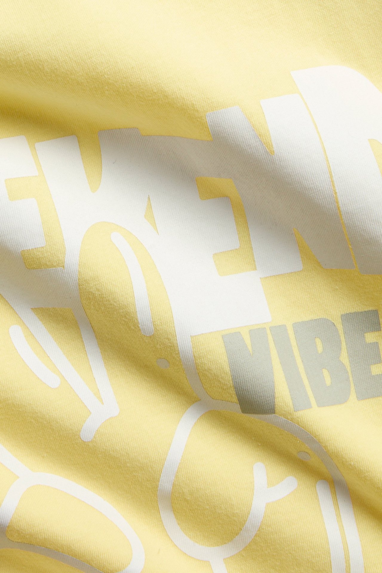 Zbliżenie żółtej bawełnianej koszulki z białym i szarym nadrukiem tekstowym z przodu.