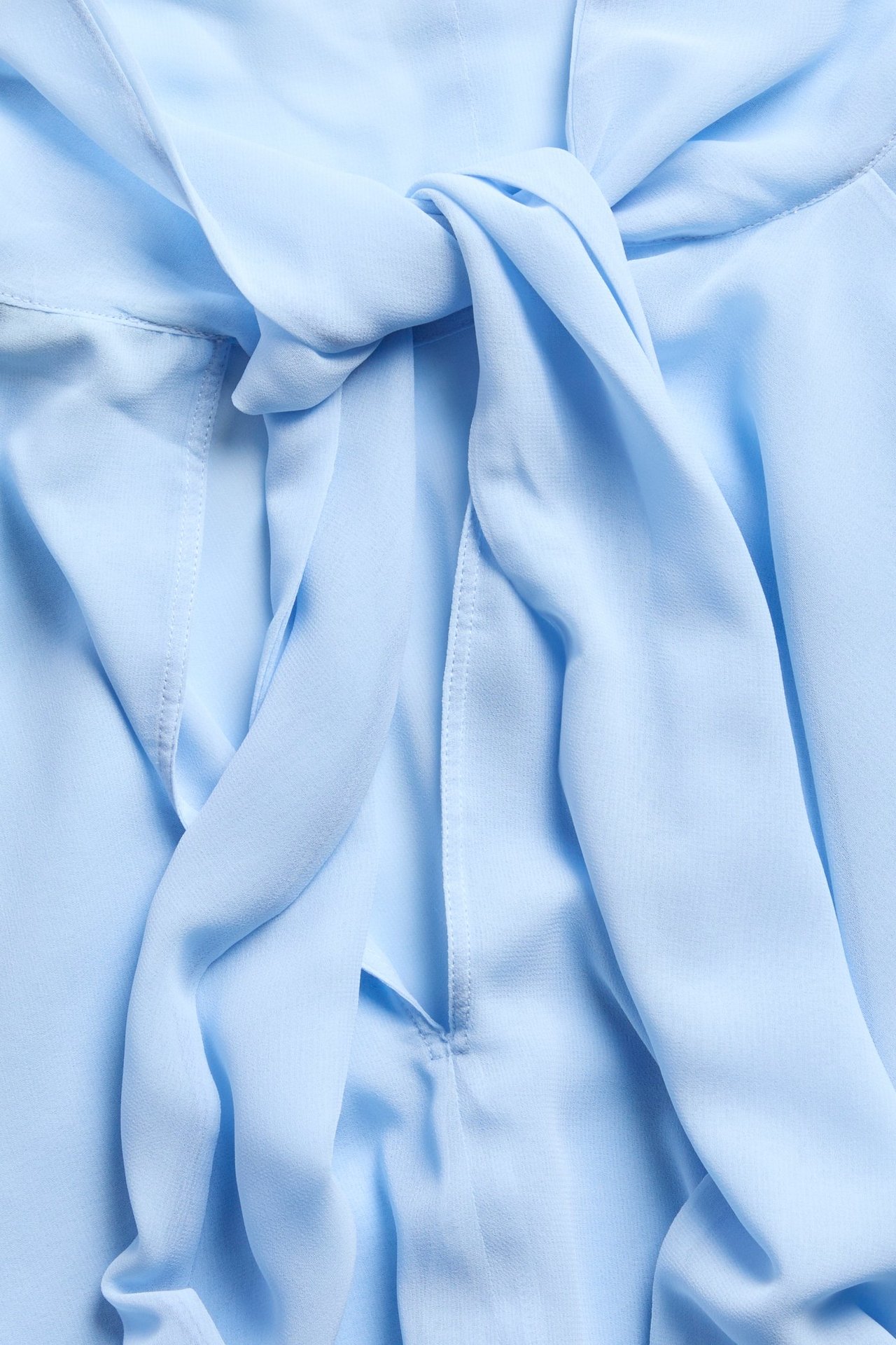 Nærbilde av en lyseblå chiffon-capebluse med en knutedetalj.