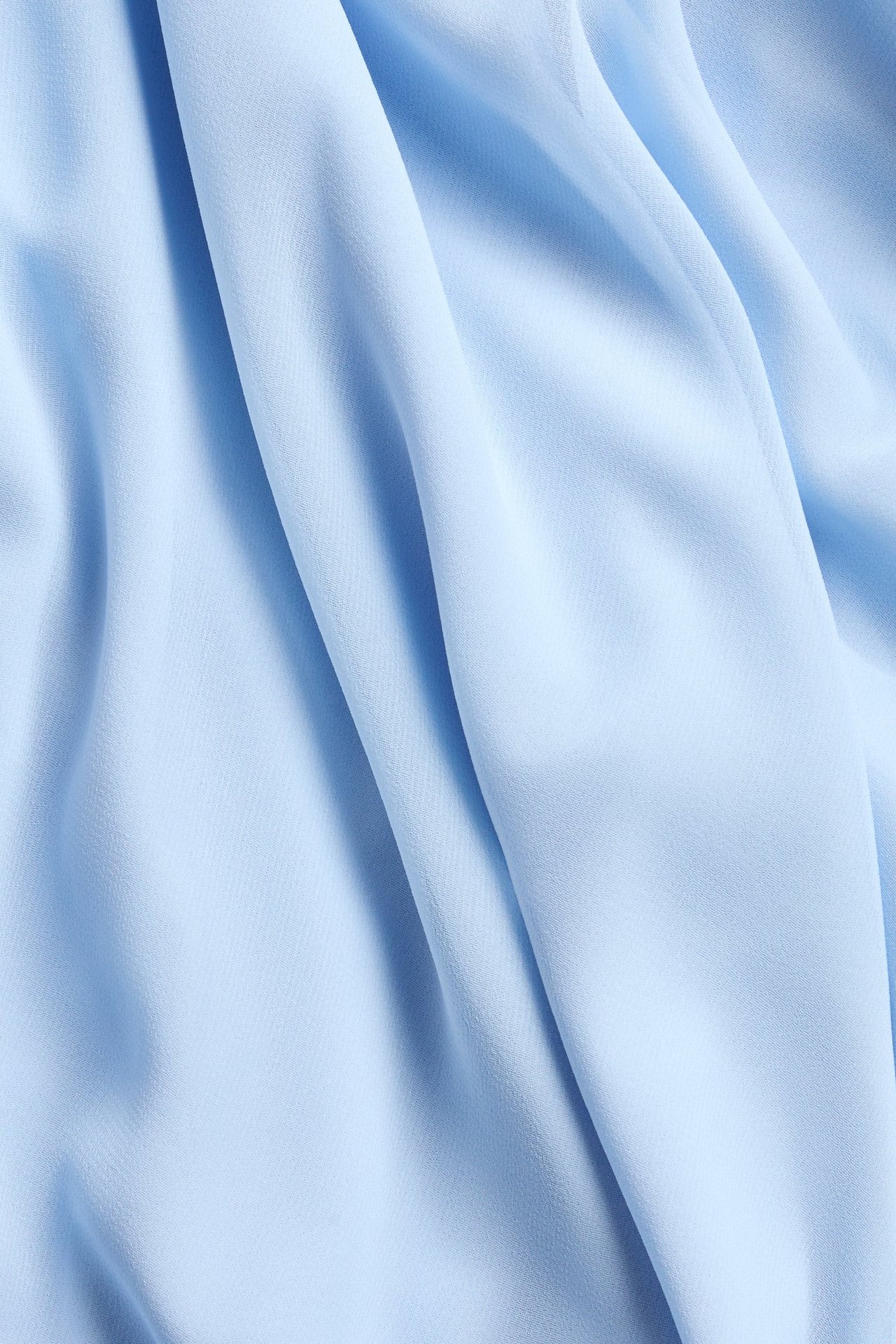 Nærbilde av lyst blått drapert chiffonstoff til et asymmetrisk skjørt.