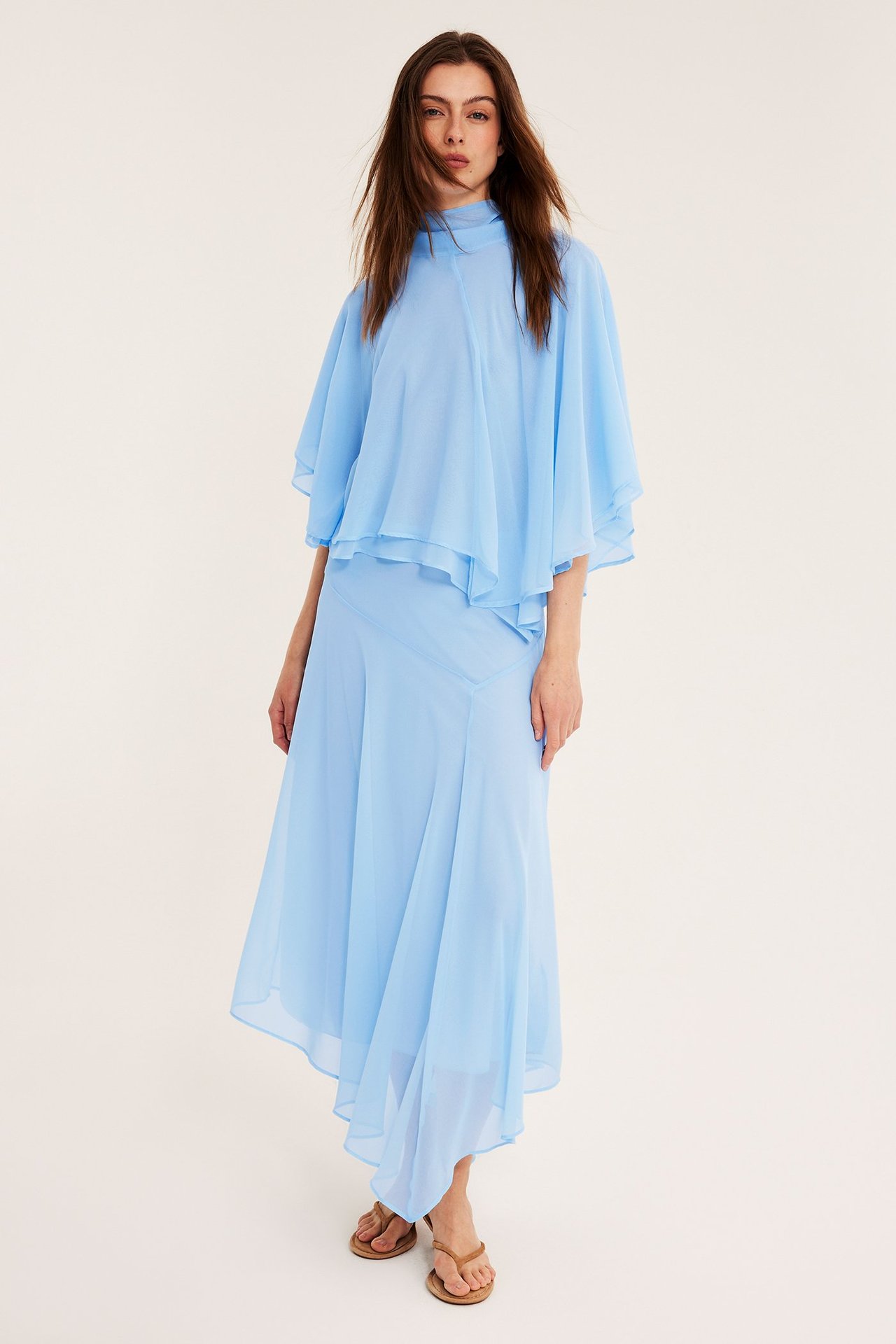 Framsida av kvinna i ljusblå asymmetrisk lång chiffongkjol, matchande topp och bruna sandaler.