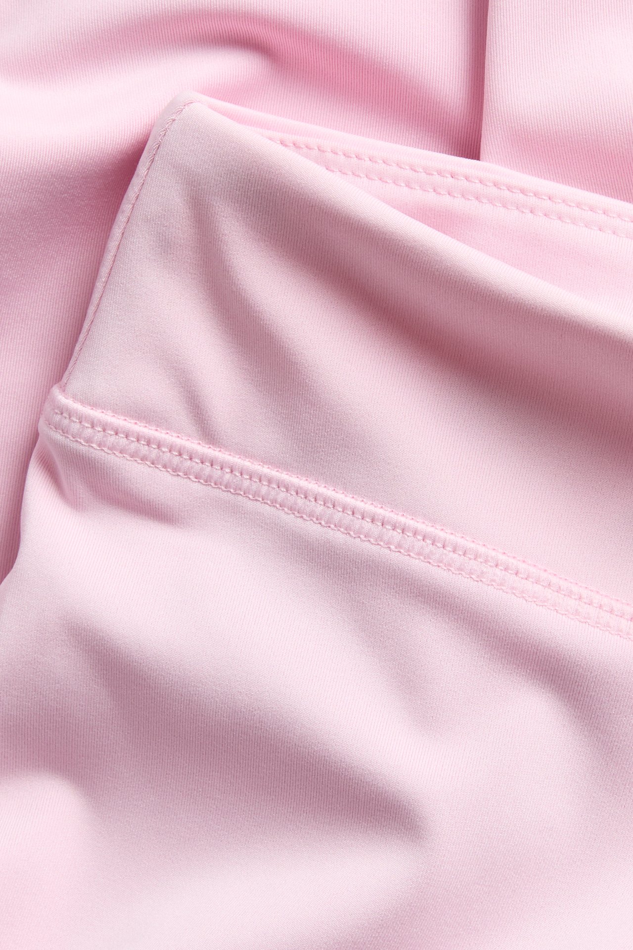 Nærbilde av rosa elastiske treningsleggings i jersey, viser linningen med sømmer.