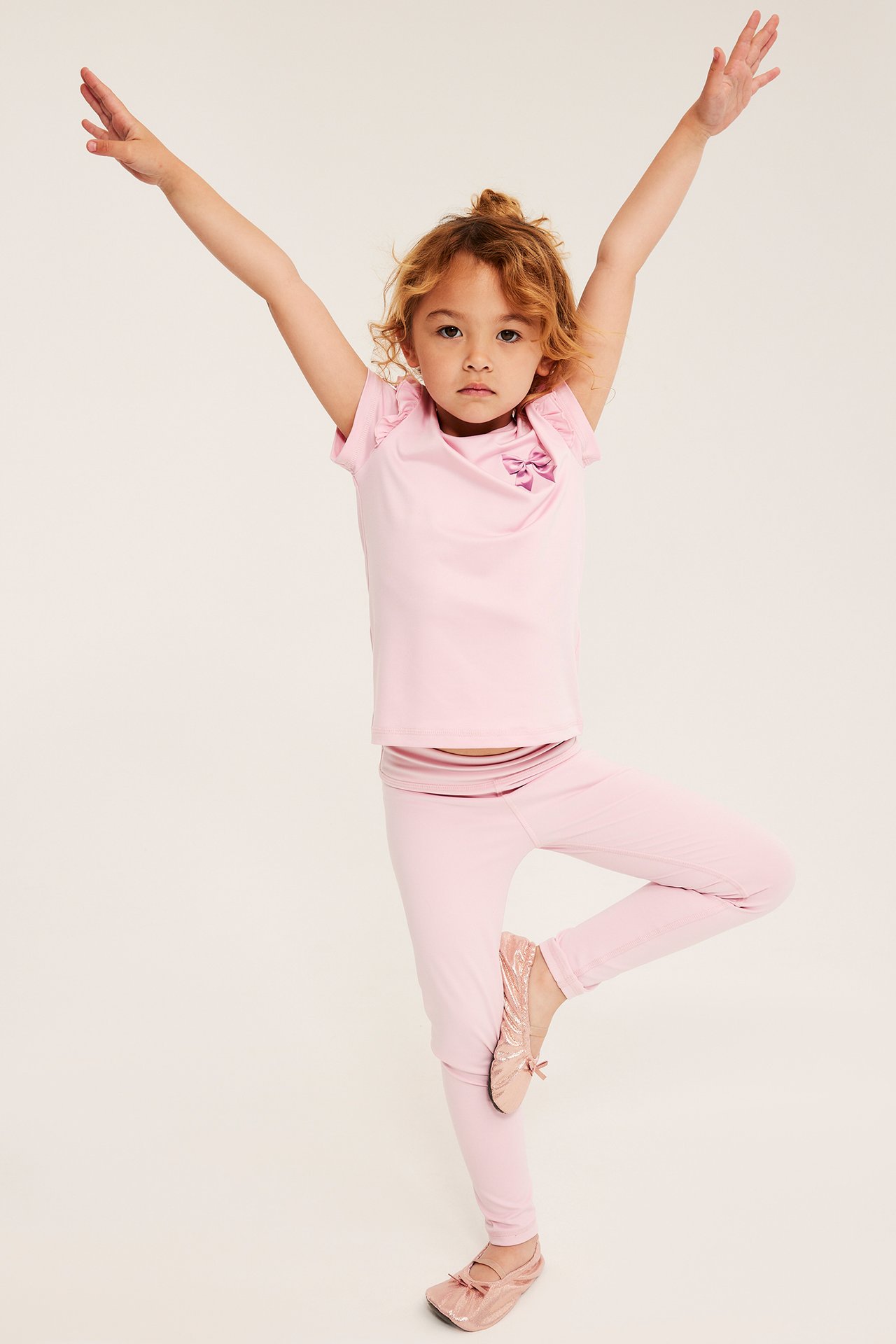 Barnegenser med kort erm, sløyfe, rosa leggings og rosa ballerinasko, forfra.