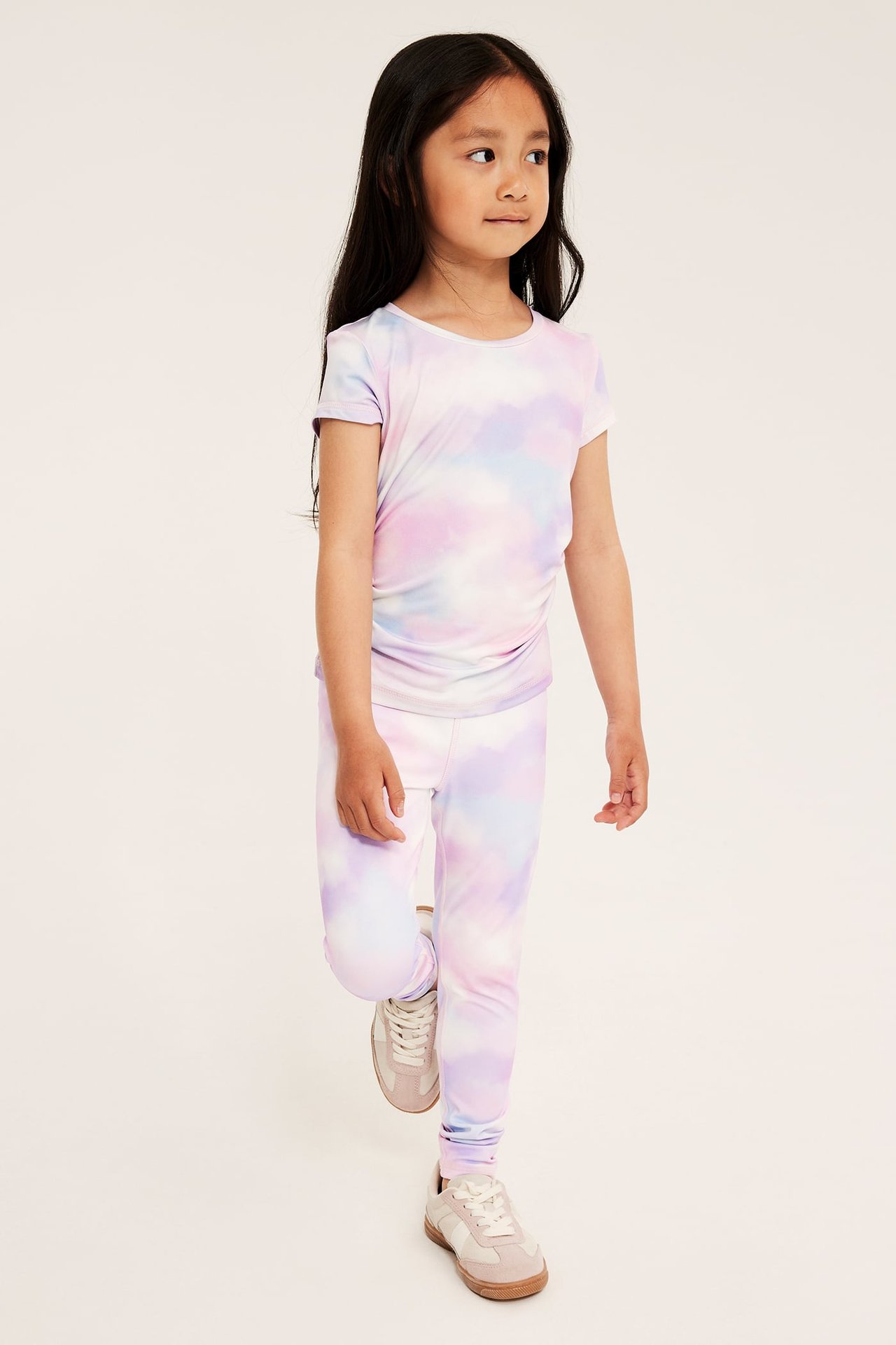 Frontvy av ett barn i off-white batikmönstrade träningsleggings och matchande t-shirt med ljusa sneakers.