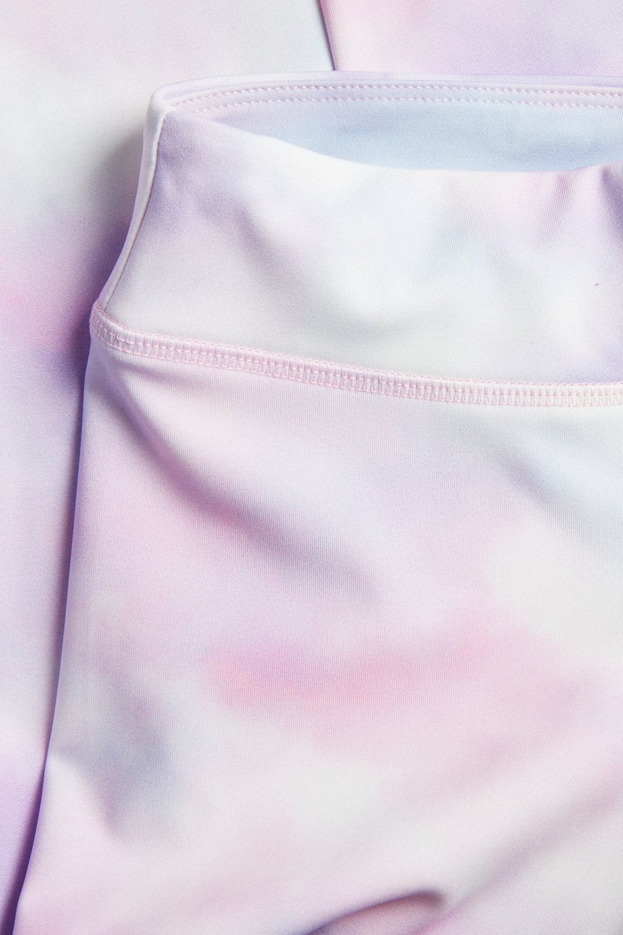 Zbliżenie elastycznych biało-różowo-fioletowych legginsów sportowych tie-dye z szerokim pasem.