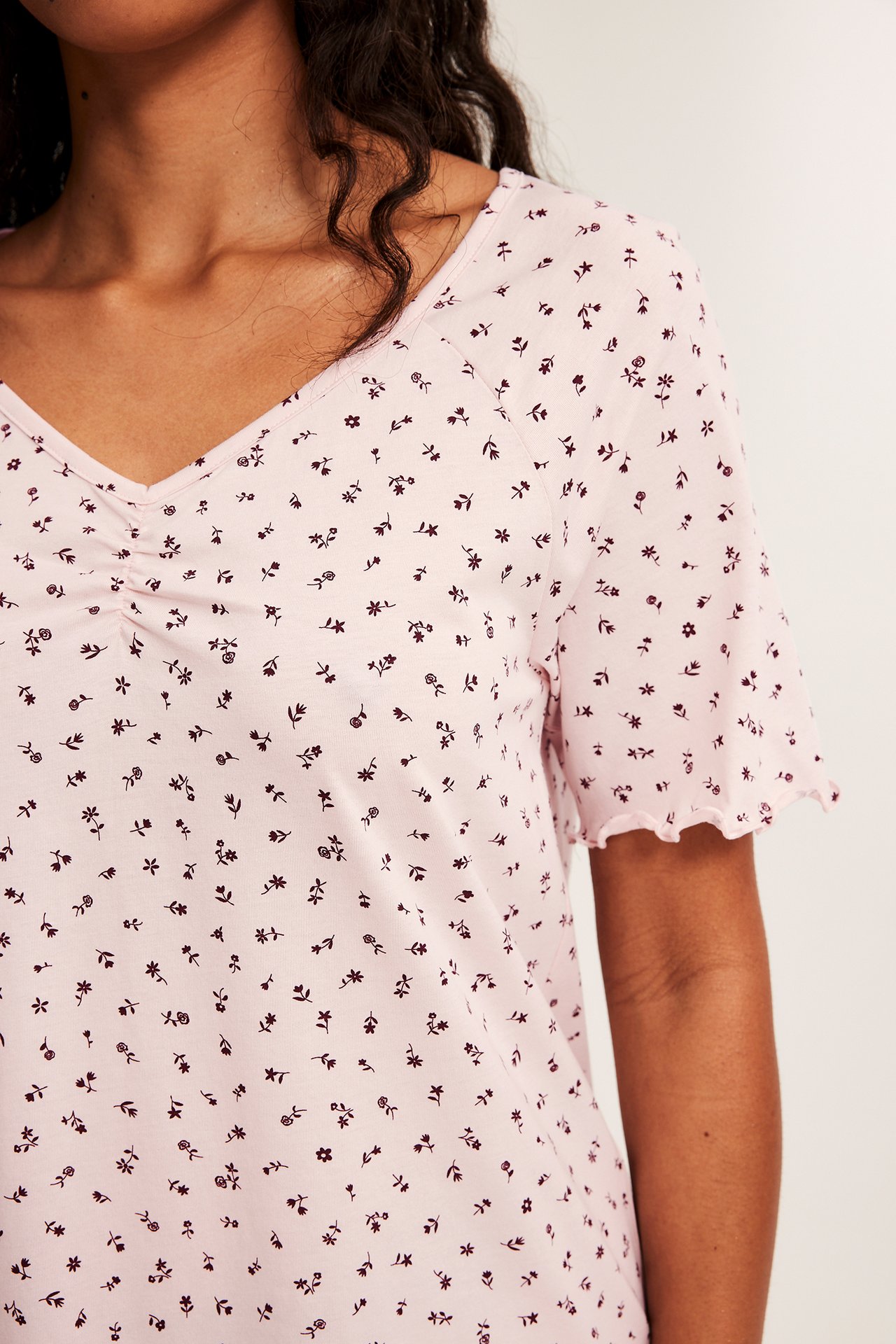 Närbild på kvinna i ljusrosa blommönstrad v-ringad t-shirt med rynkad front och volangärmar.