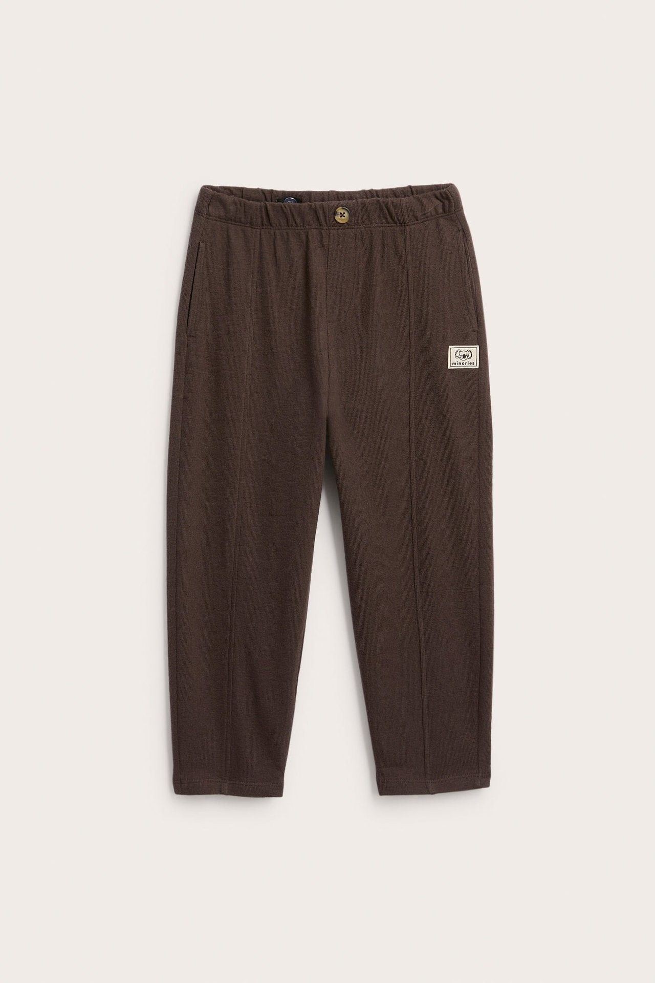Frontvisning av brune joggebukser med elastisk midje, knapp og dekorativt merke.