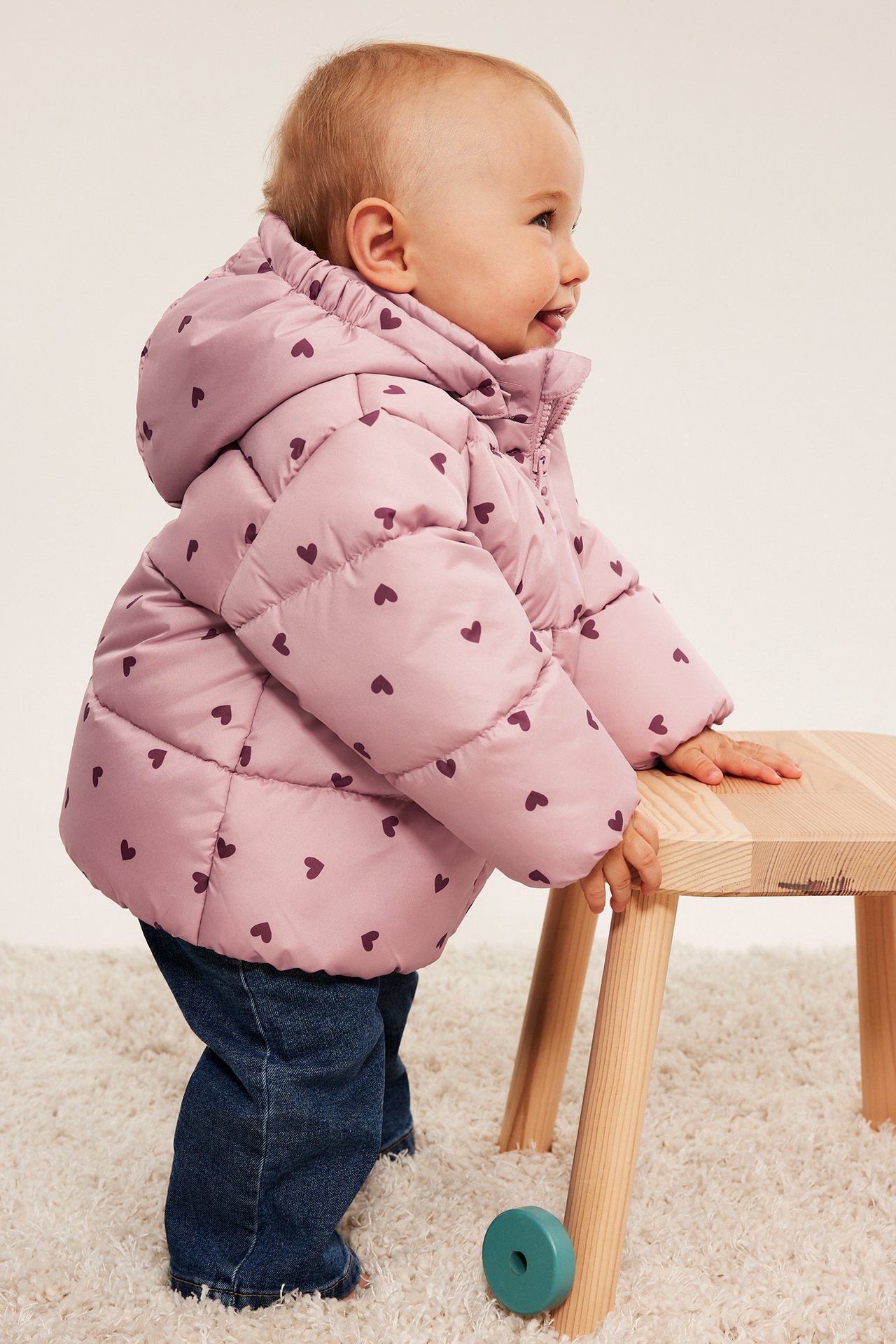 Sidovy av baby i rosa hjärtmönstrad puffjacka med blå jeans.