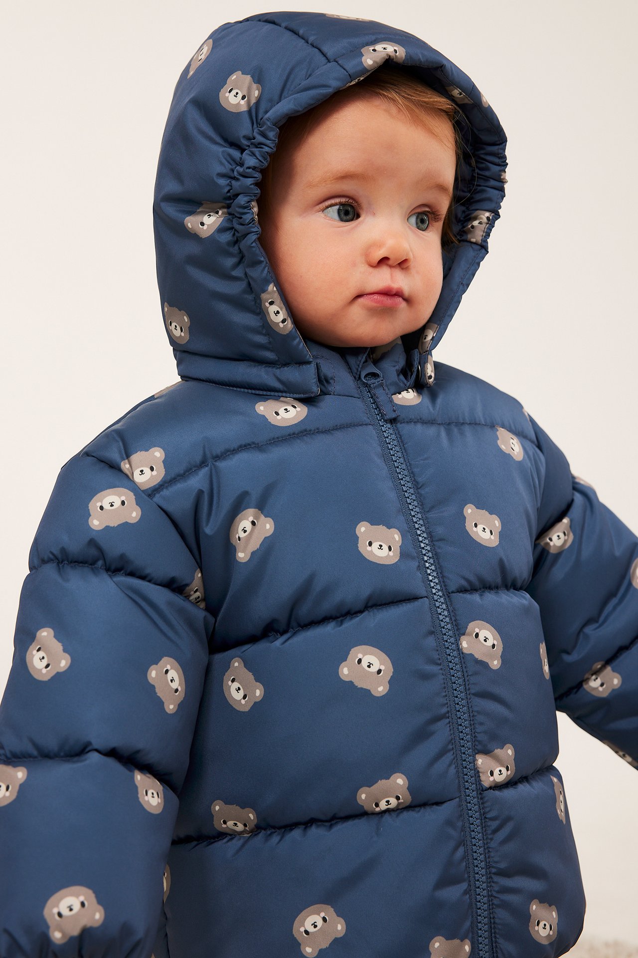 Närbild på baby i blå huvförsedd pufferjacka med nallemönster.