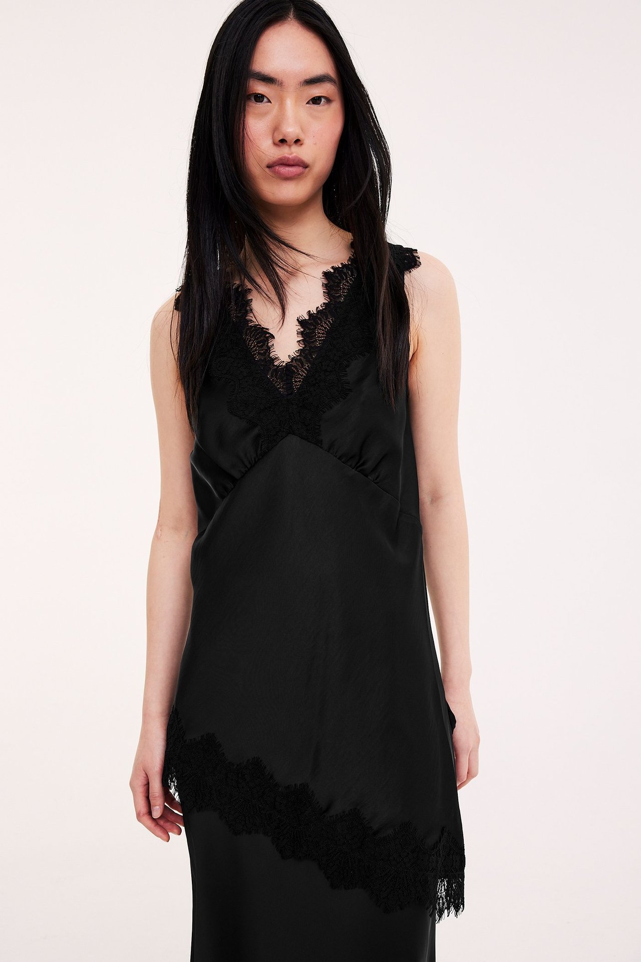 Frontvy av kvinna i svart satinlinne med spetskant vid V-ringning och nederkant.