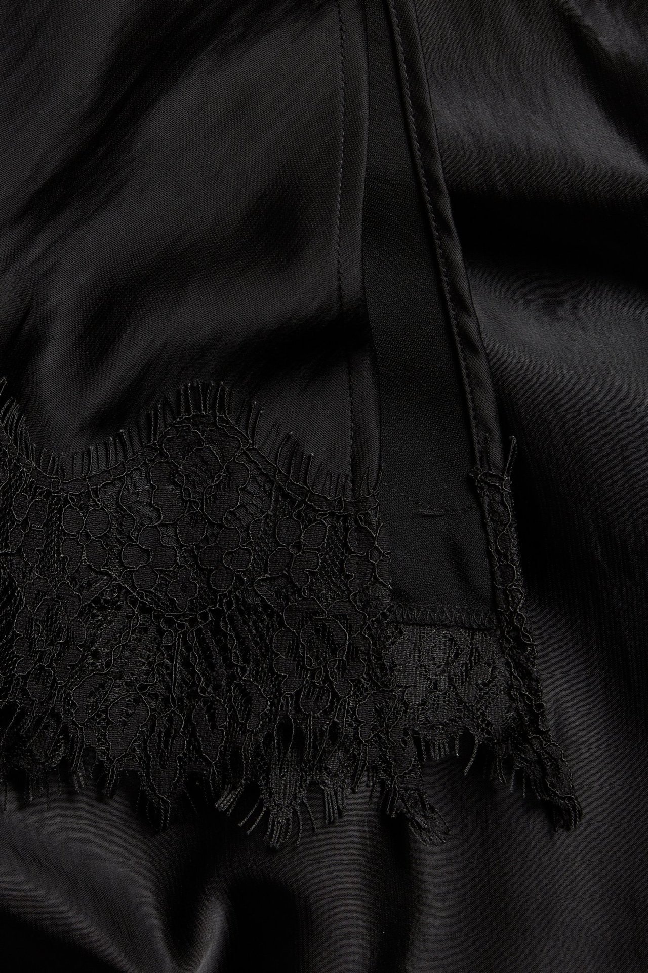 Zbliżenie na czarny satynowy top z misterną czarną koronką.