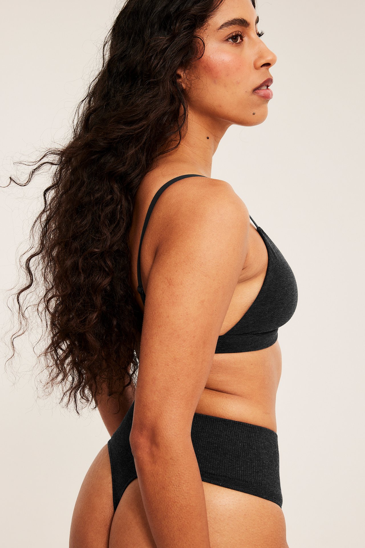 Sidebilde av kvinnelig modell i mørkegrå ribbet bralette og matchende høy midje truse.
