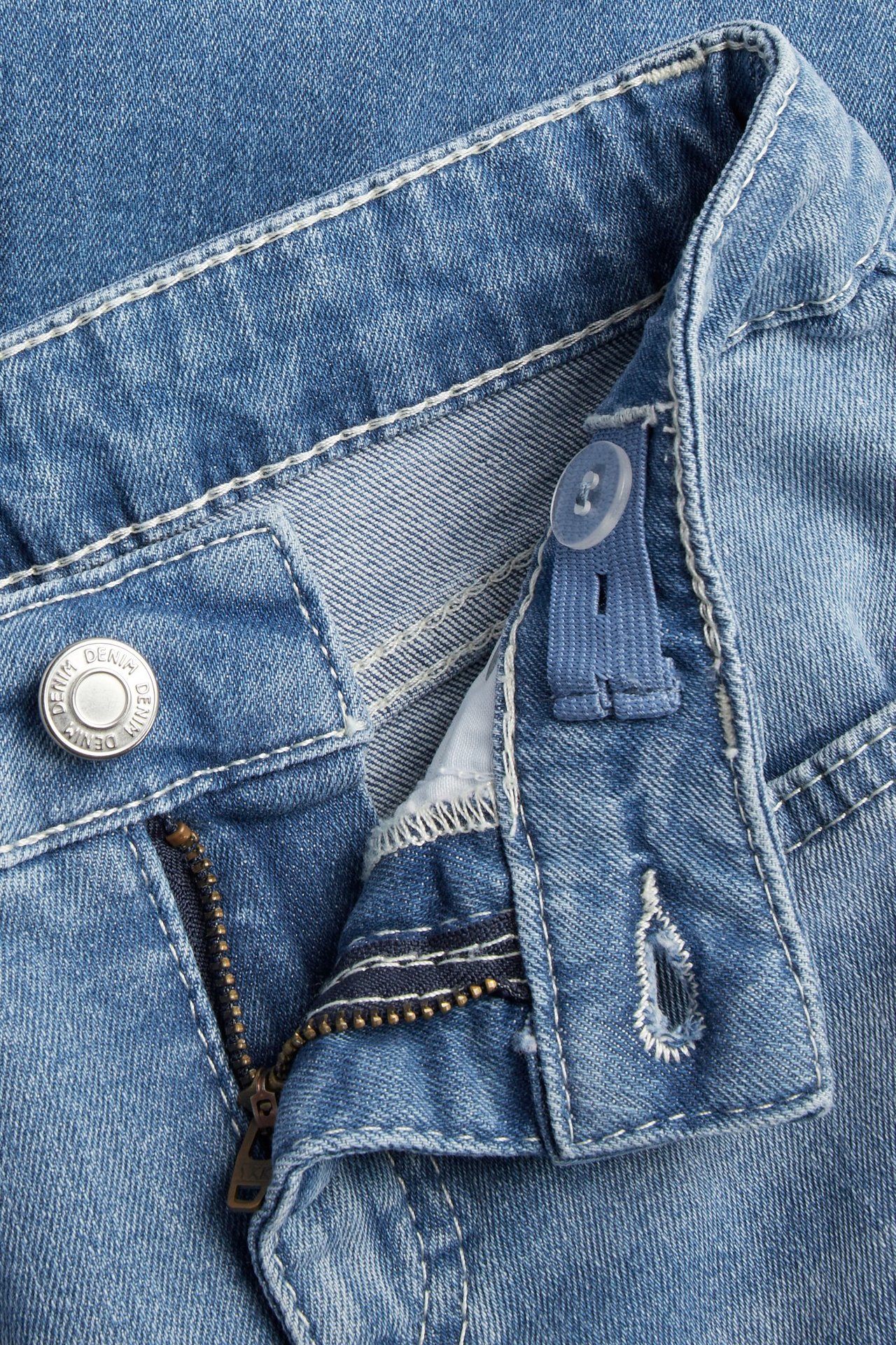 Zbliżenie na jasnoniebieskie jeansy bootcut z otwartym zamkiem i regulowaną talią na guzik.