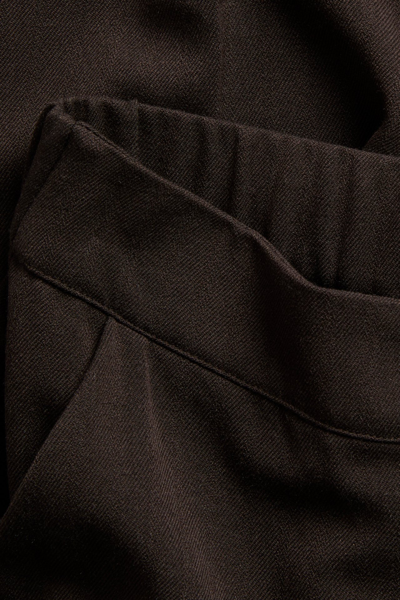 Zbliżenie na ciemnobrązowy materiał twill o skośnym splocie i widocznym szwie.