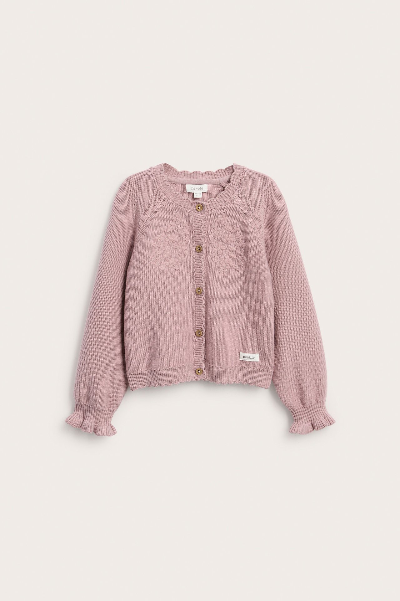 Framifrån en rosa stickad kofta för barn med blommigt broderi, knäppning fram och volangmuddar.