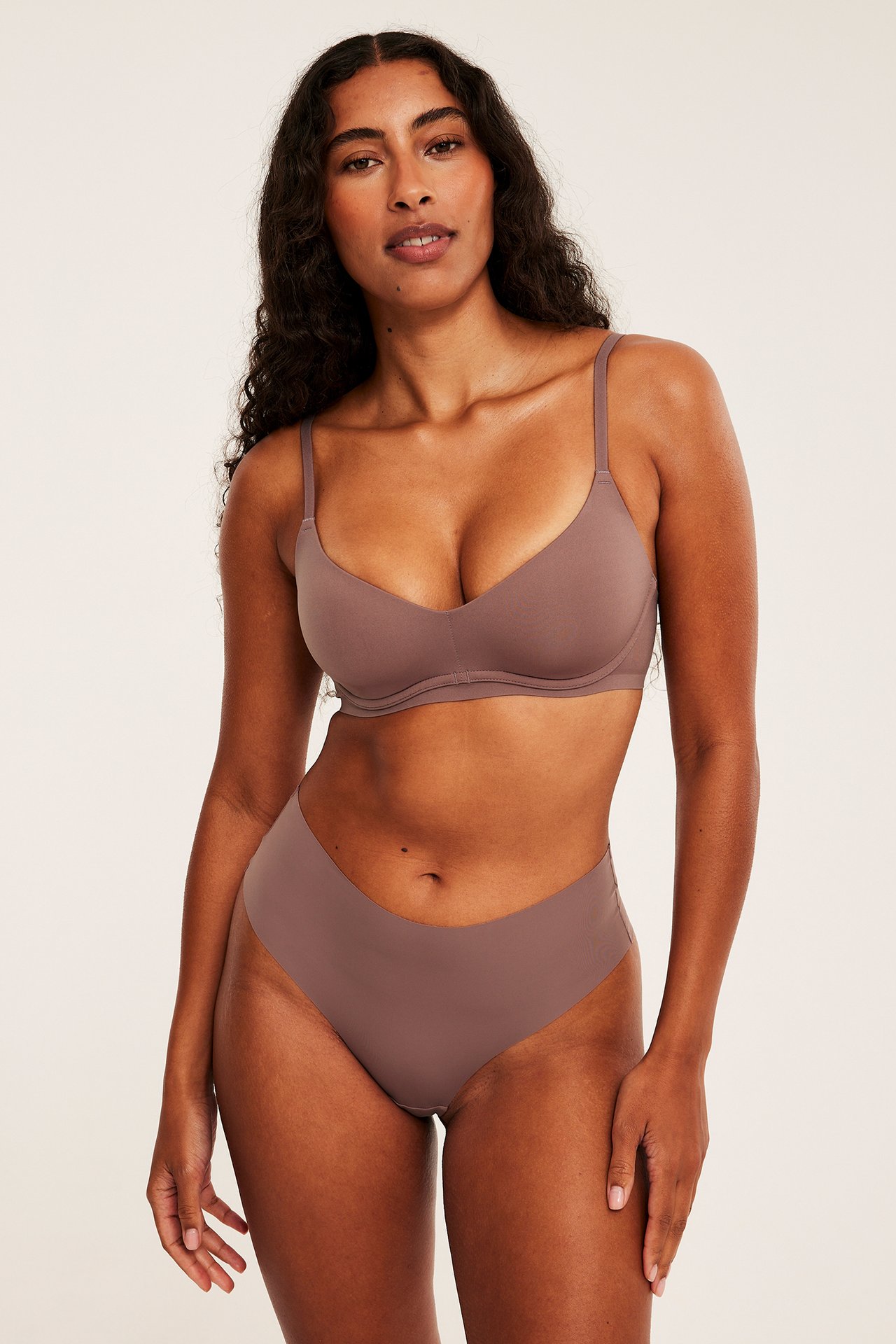 Framifrån, kvinna i vadderad mauve plunge-bh och matchande högskuren trosa.