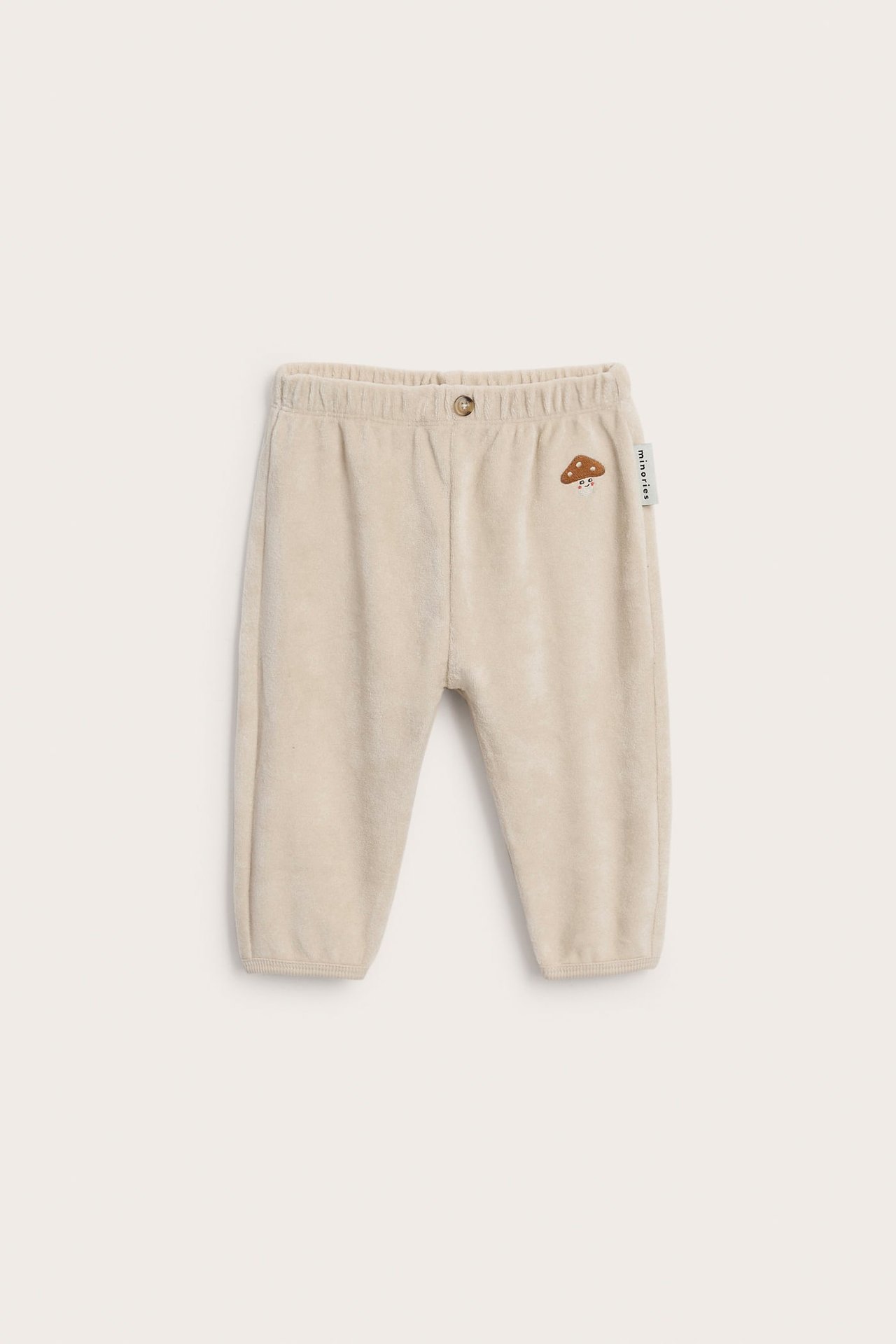 Front av babybukse i beige velur med elastisk midje, knapp og soppbroderi.
