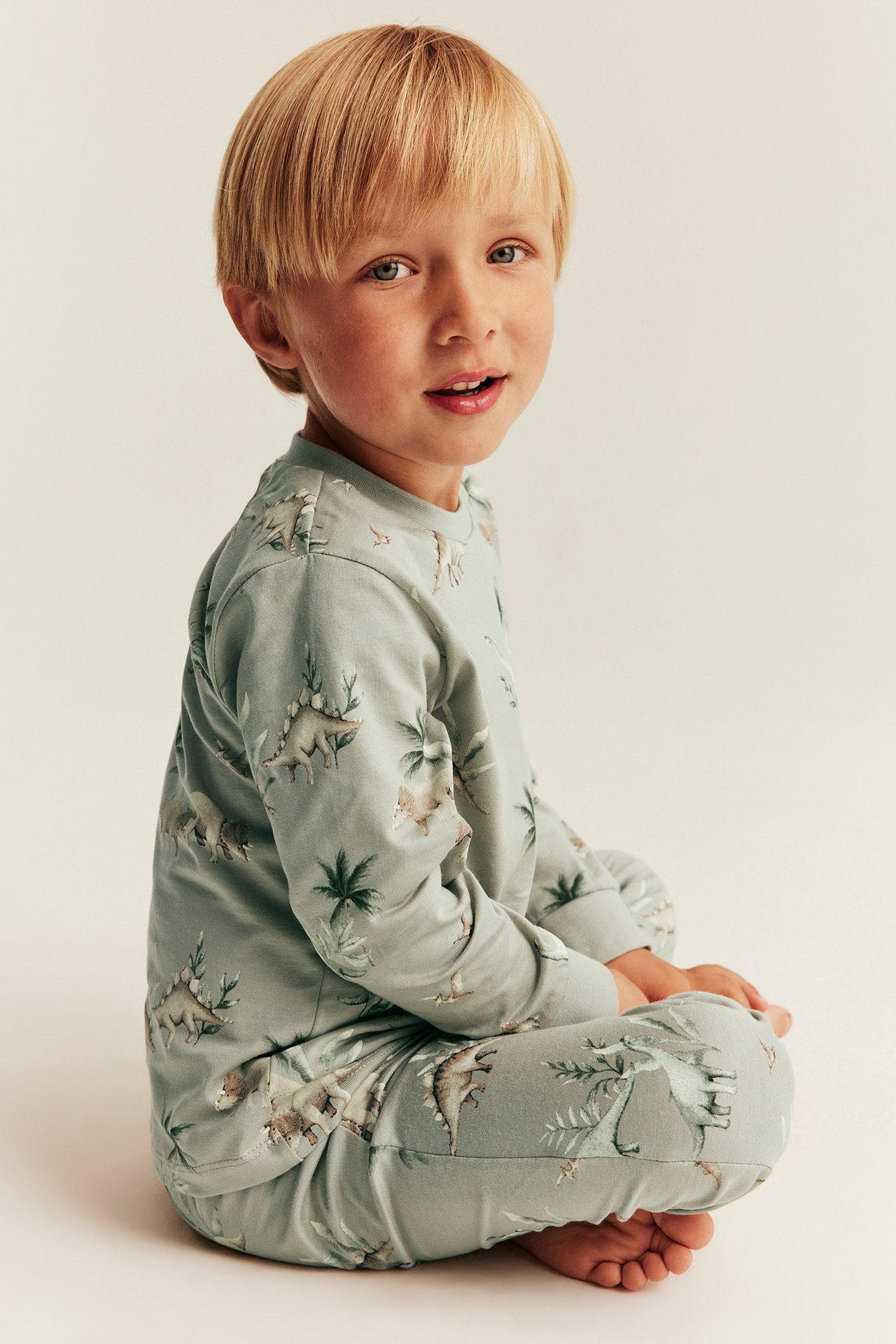 Sivukuva lapsesta, jolla on vaaleanvihreä kaksiosainen puuvillapyjama dinosauruskuviolla.
