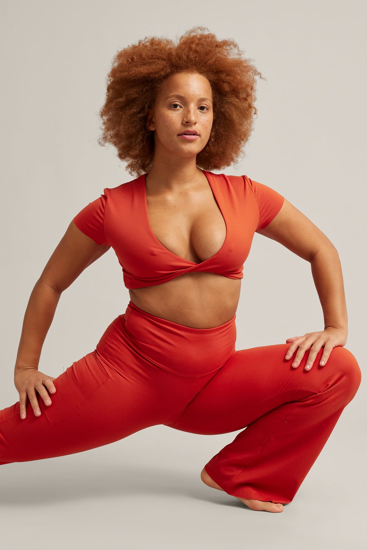 Framsida av kvinnlig modell i roströd vriden crop top och matchande utsvängda yogabyxor.