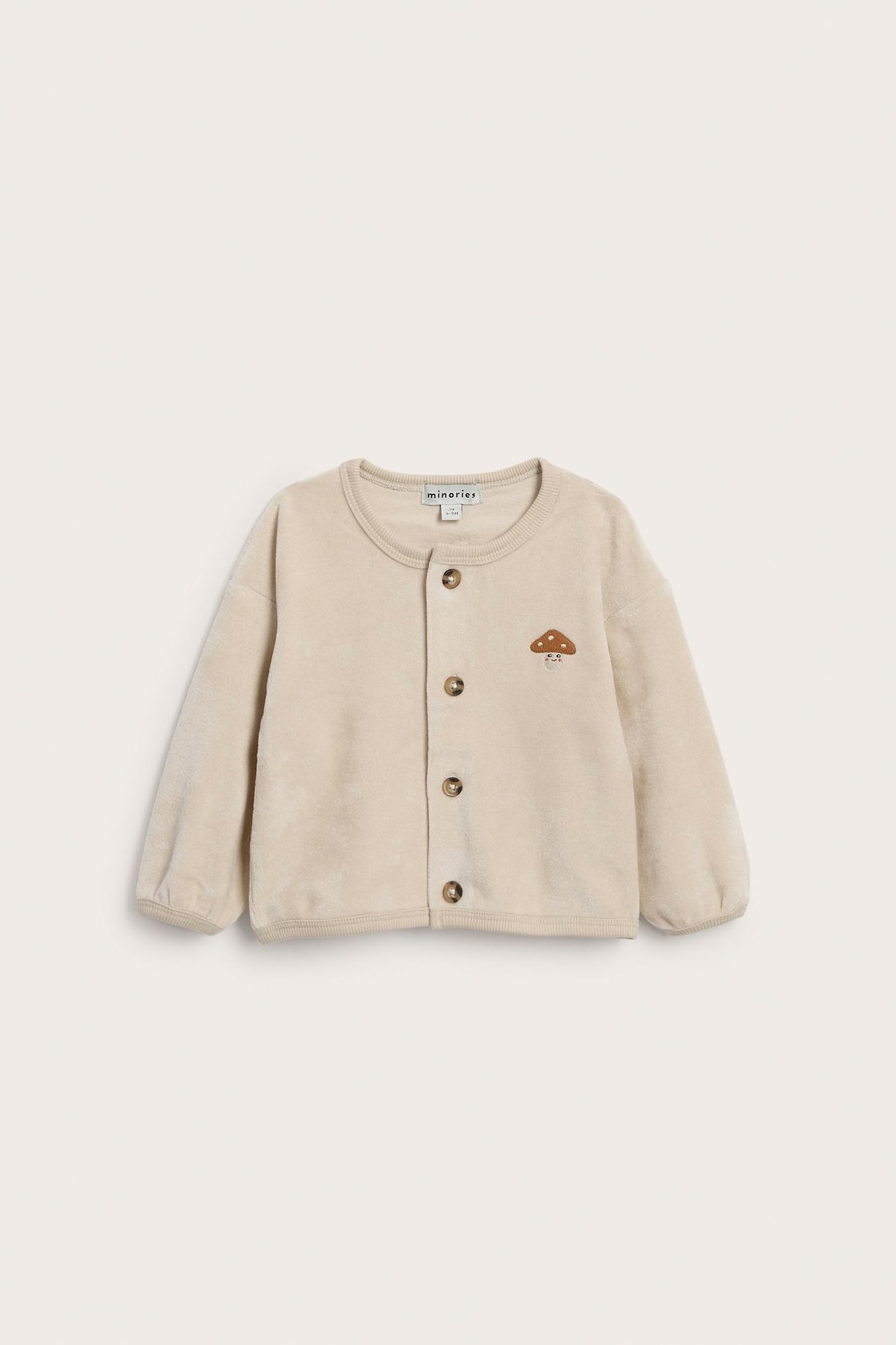 Forfra av lys beige babyjakke med soppbroderi og fem brune knapper.