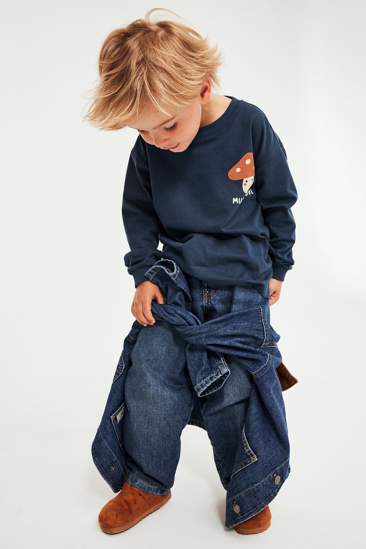 Front: barn i mørkeblå langermet genser med soppmønster, jeans, jakke og brune tøfler.