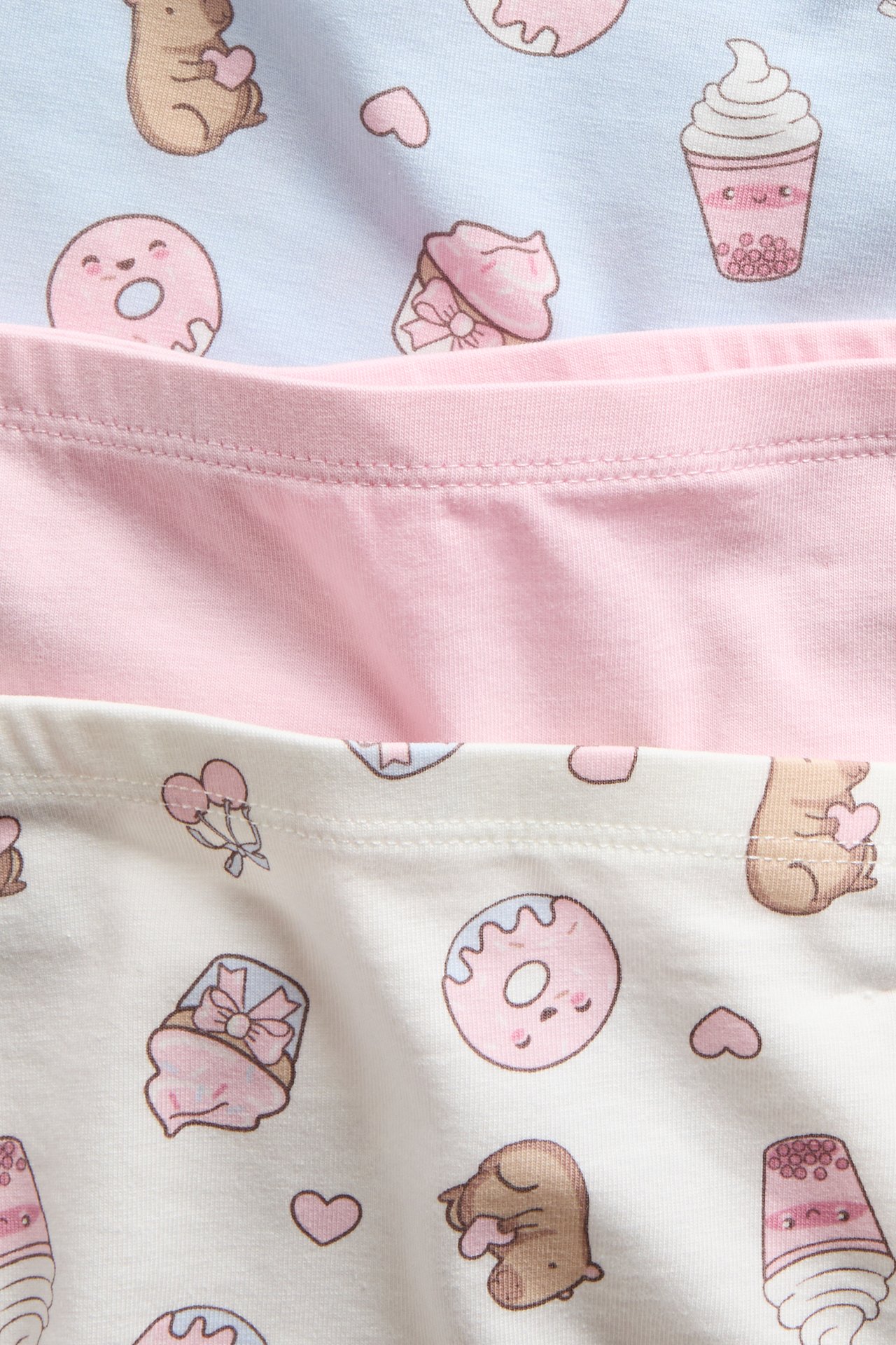 Lähikuva lasten 3-pack puuvillabokserishortseista: pinkki, luonnonvalkoinen ja vaaleansininen dessertkuviolla.