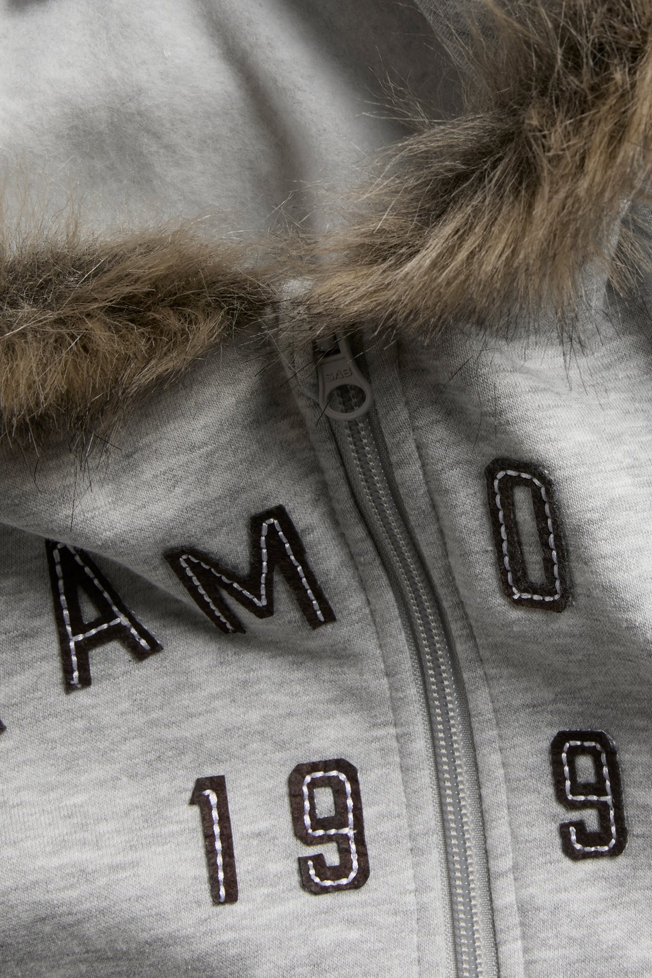 Närbild av en gråmelerad huvtröja med dragkedja, fuskpäls och broderade detaljer på framsidan.