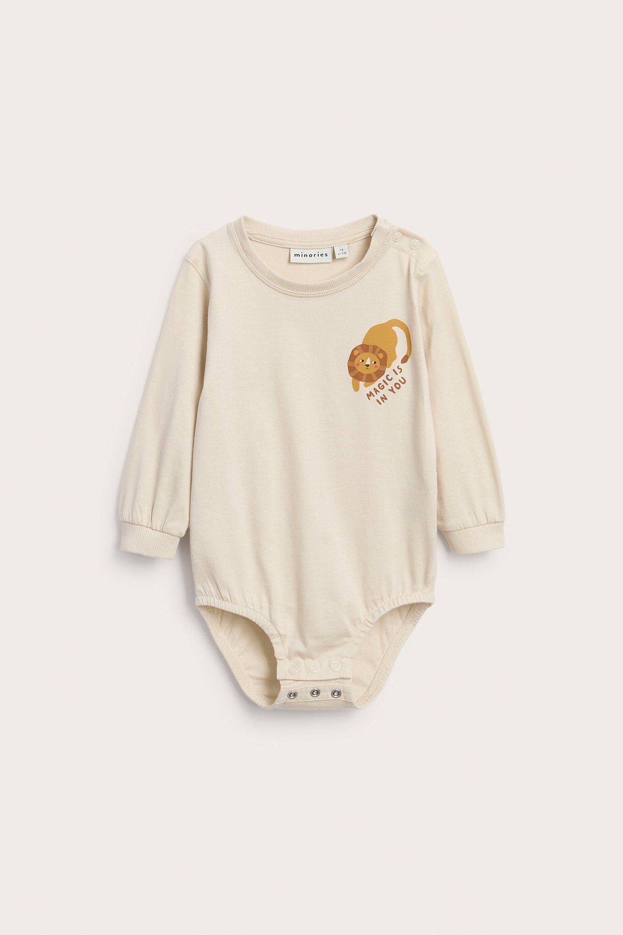 Front av beige langermet babybody med løvetrykk og teksten 'MAGIC IS IN YOU'.