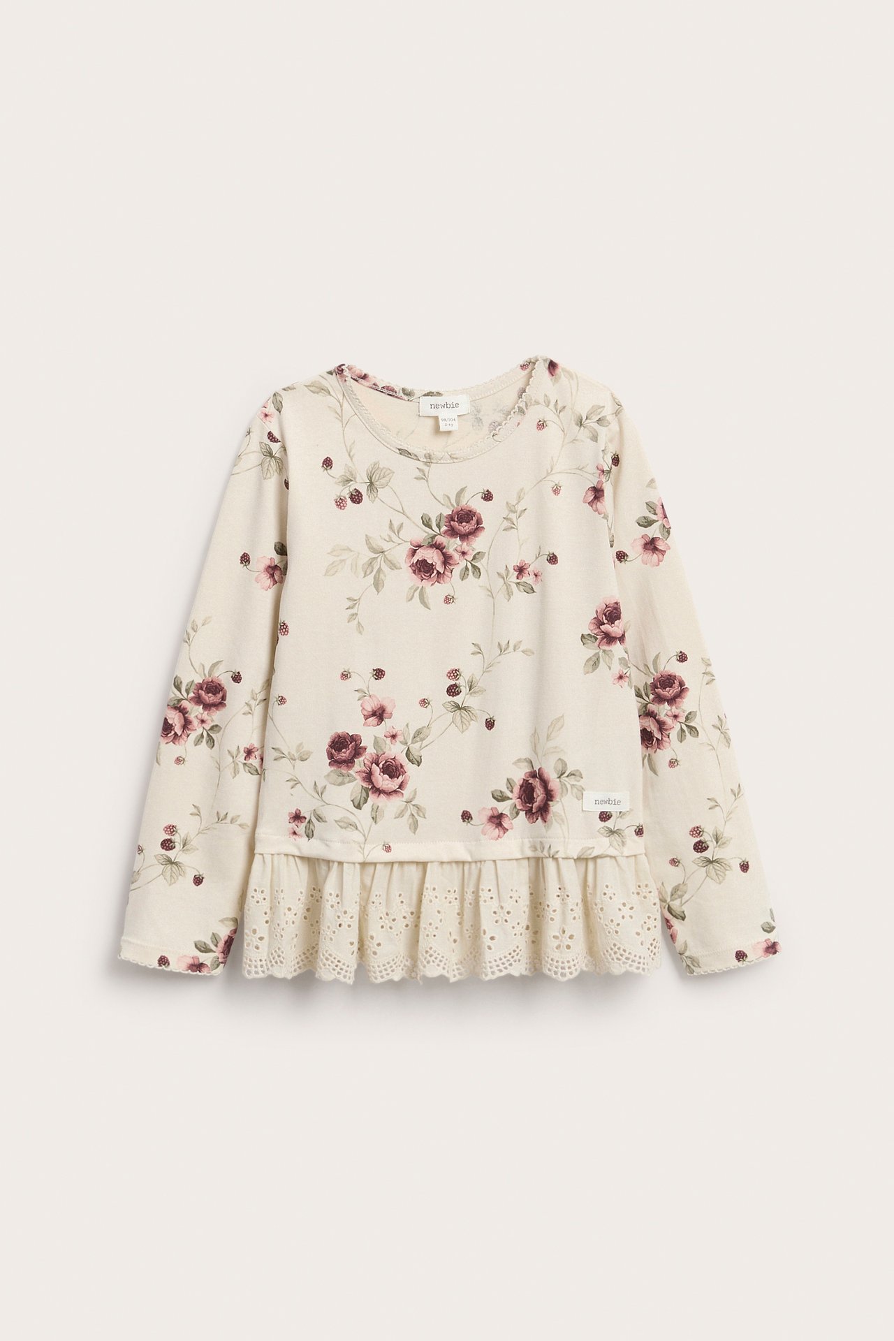 Frontbilde av en barne-topp i kremfarge med lange ermer, blomstertrykk og blondekant.
