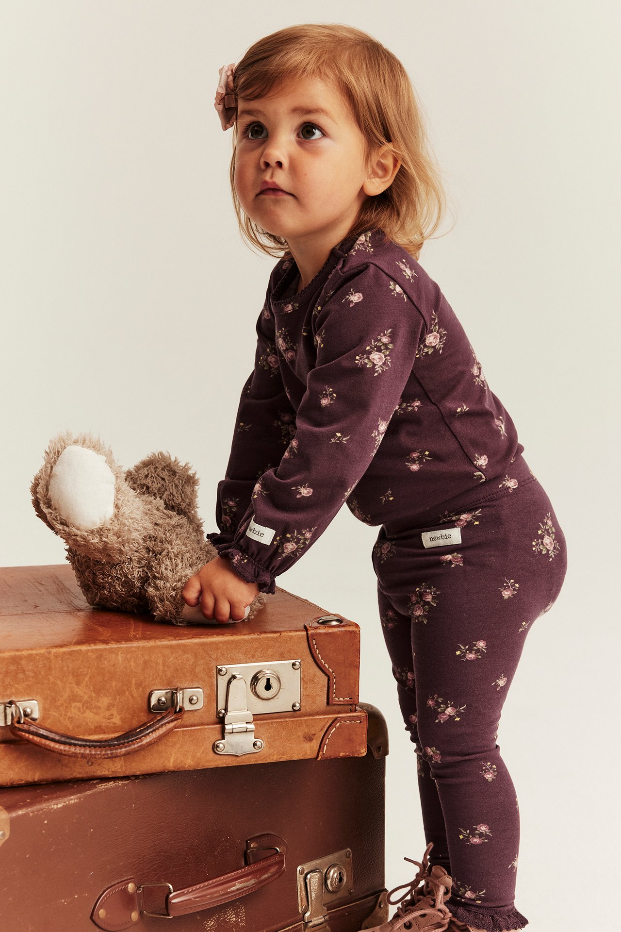 Barn i mørk lilla blomstret langermet topp og leggingssett, berører bamse.
