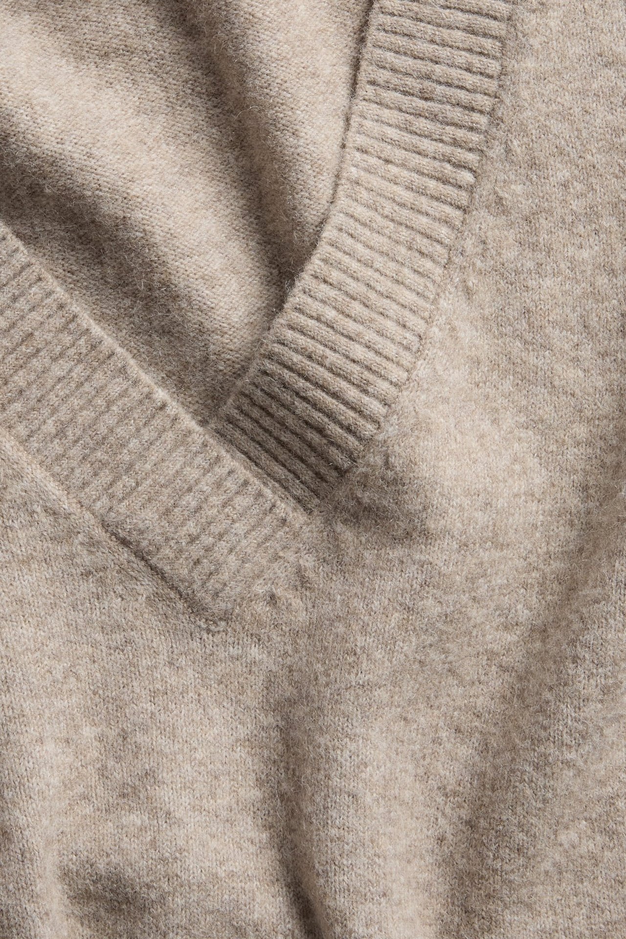 Nærbilde av en myk beige V-hals strikkegenser.