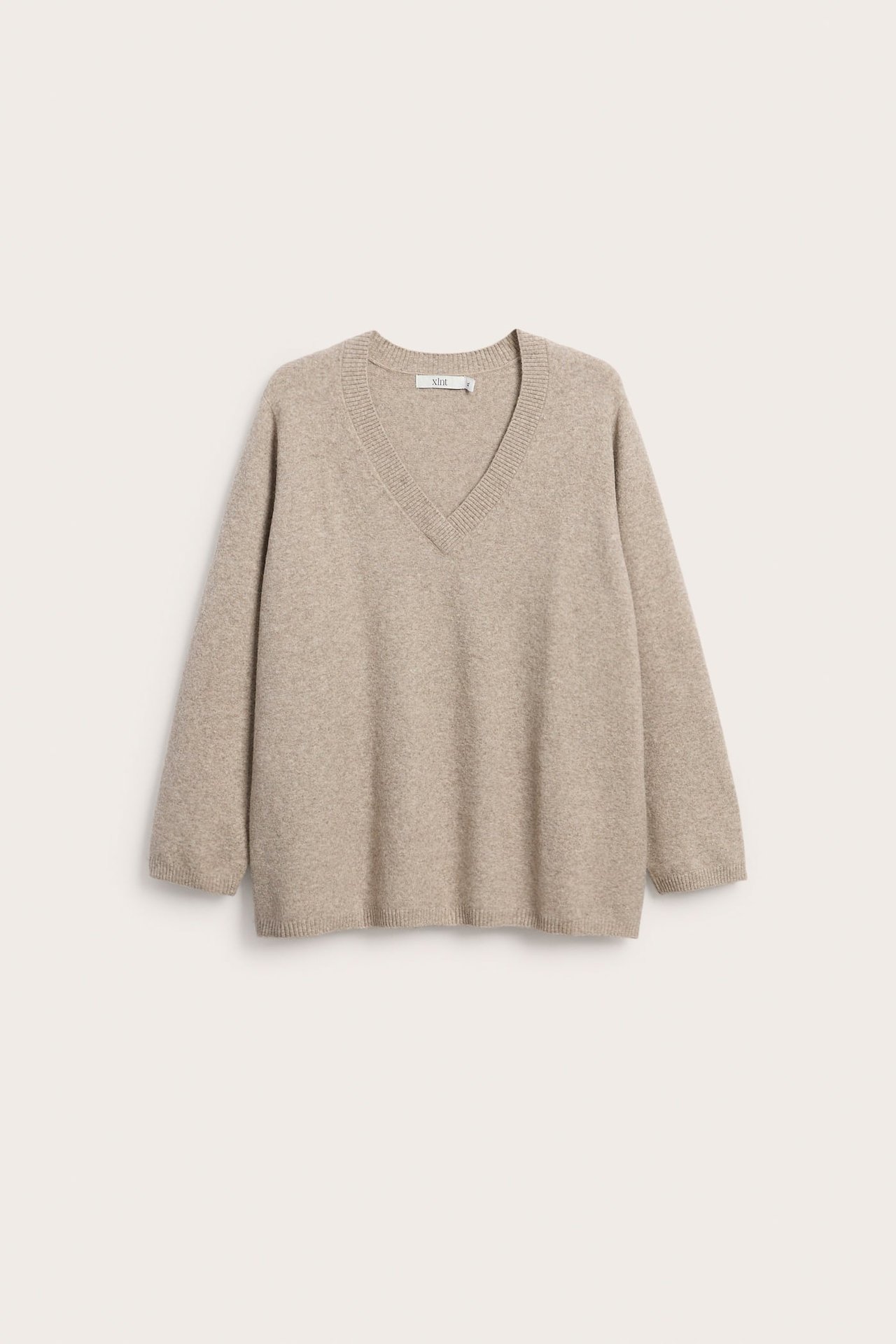 Forfra, en lys beige V-halset strikkegenser med lange ermer.